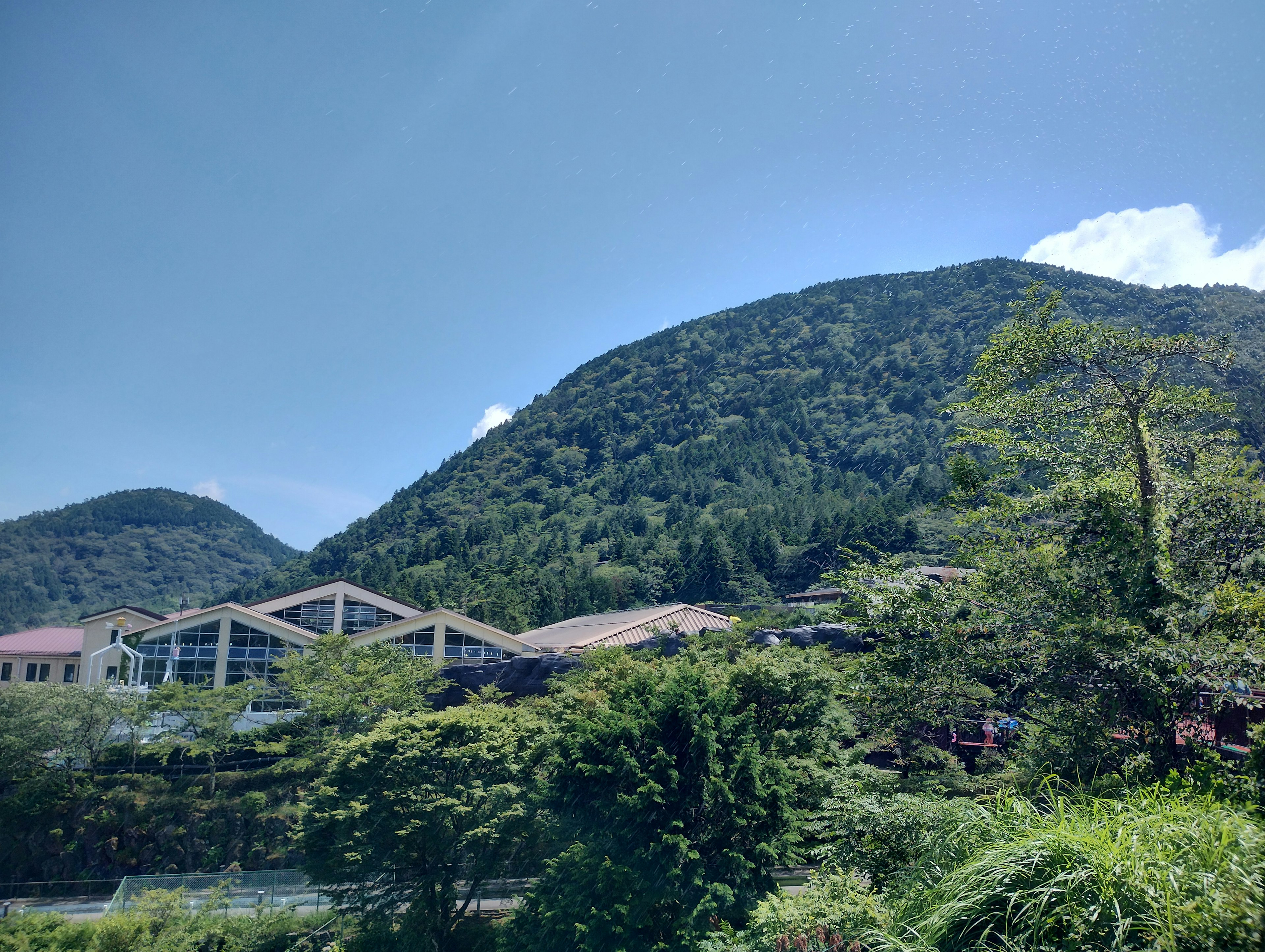 Lush green mountain landscape with buildings under a clear blue sky