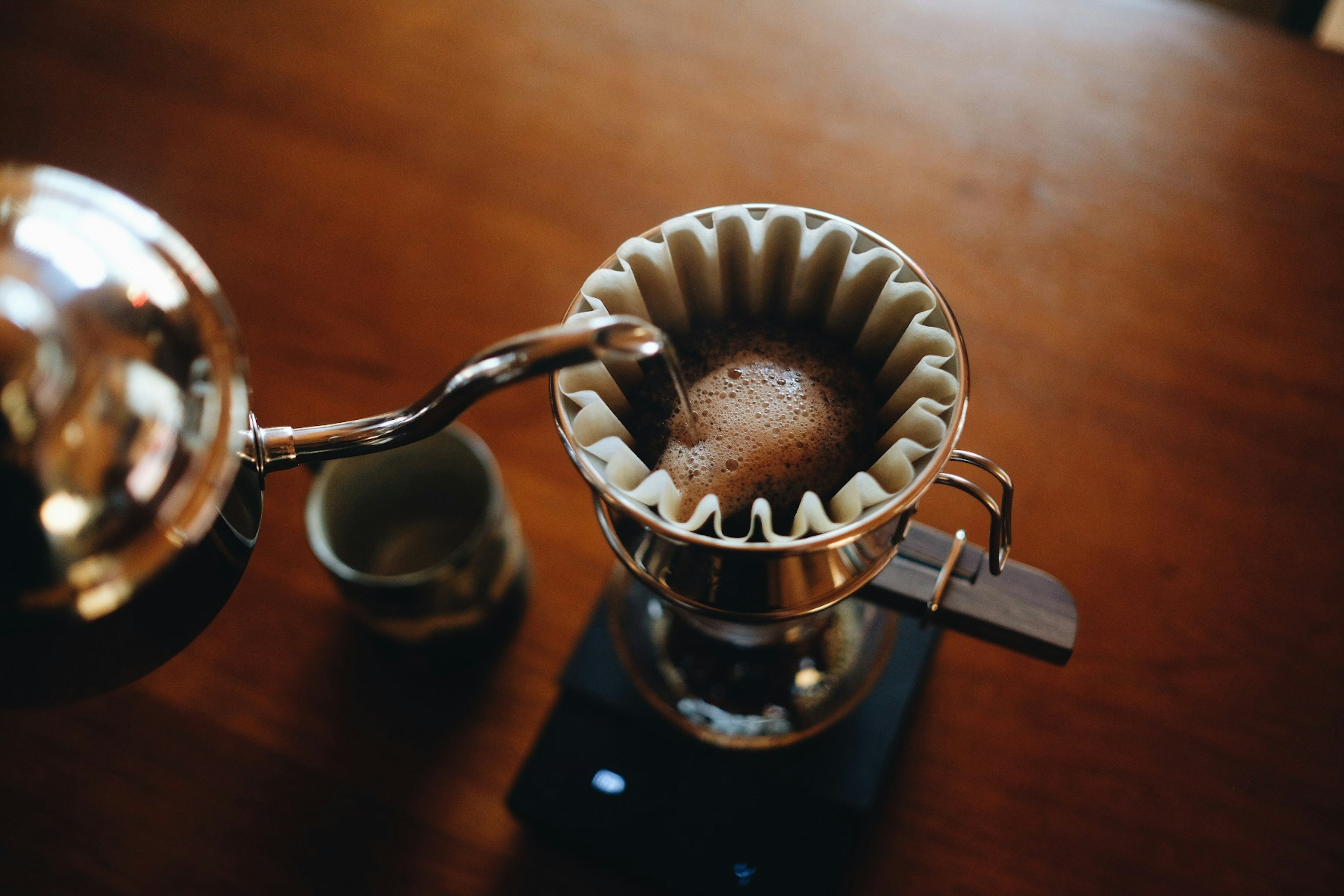 Heißes Wasser in einen Kaffeefilter gießen mit einer Tasse in der Nähe