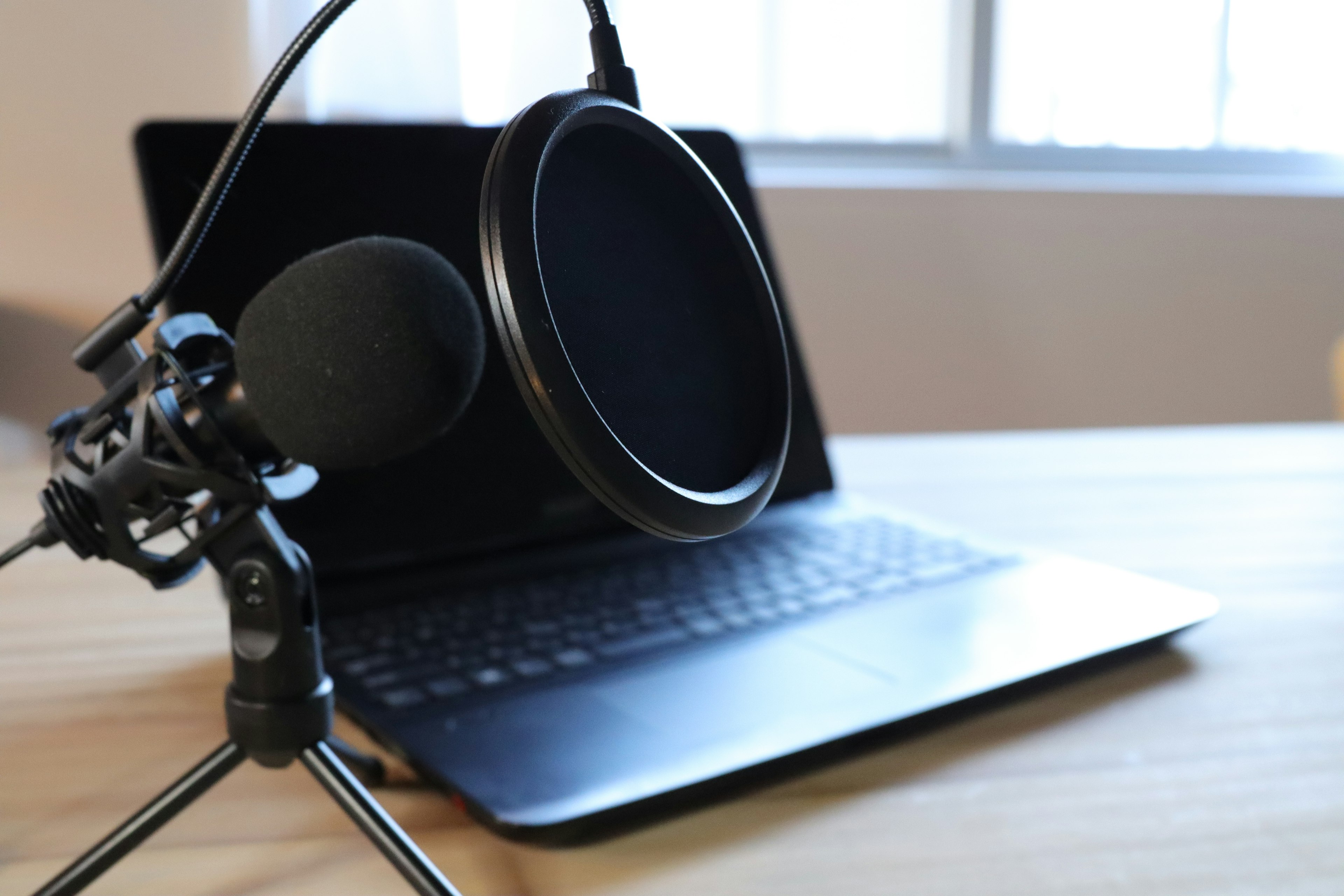 Close-up of a microphone and pop filter in front of a laptop