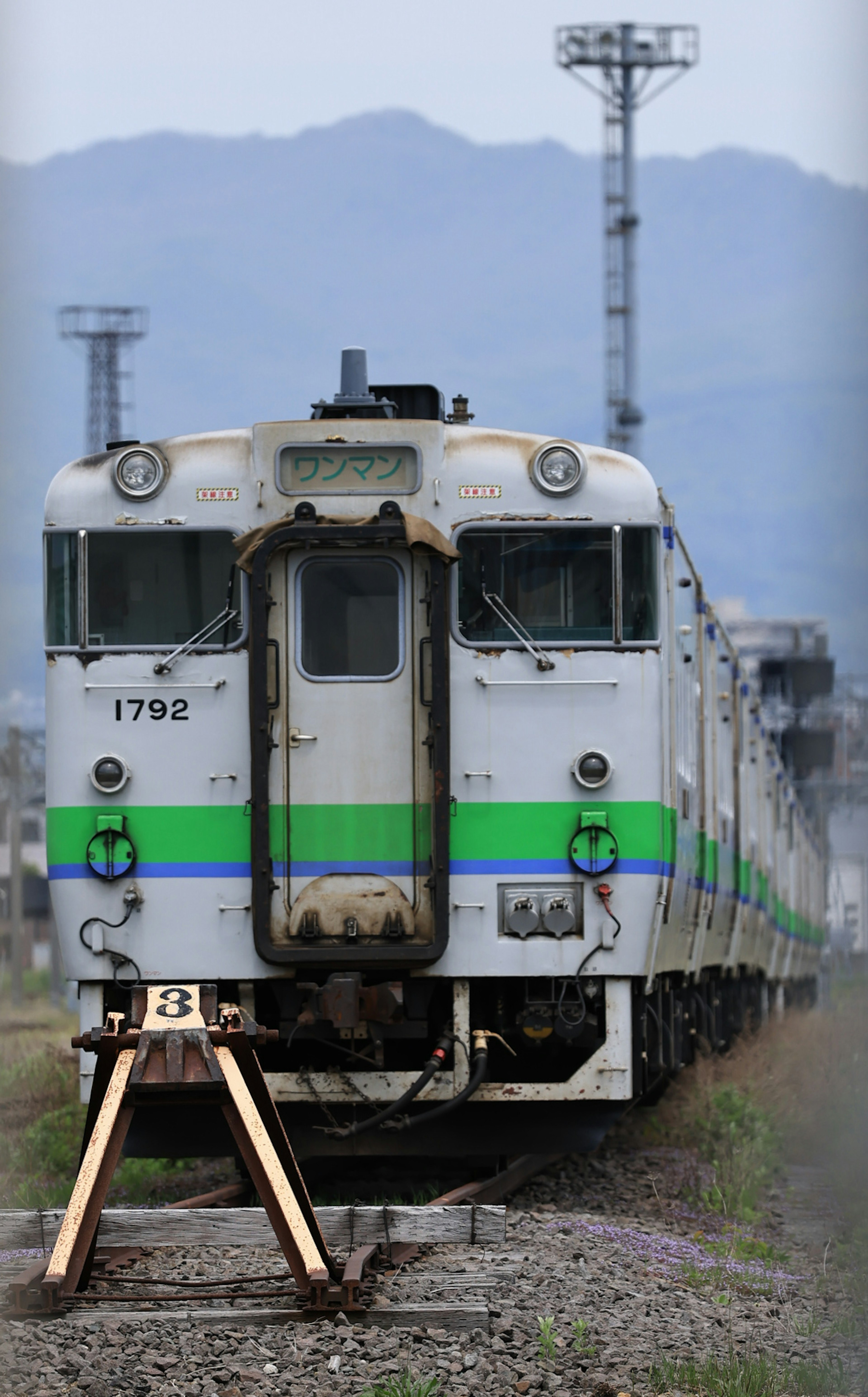 An old train with green stripes parked on the tracks in a rural setting