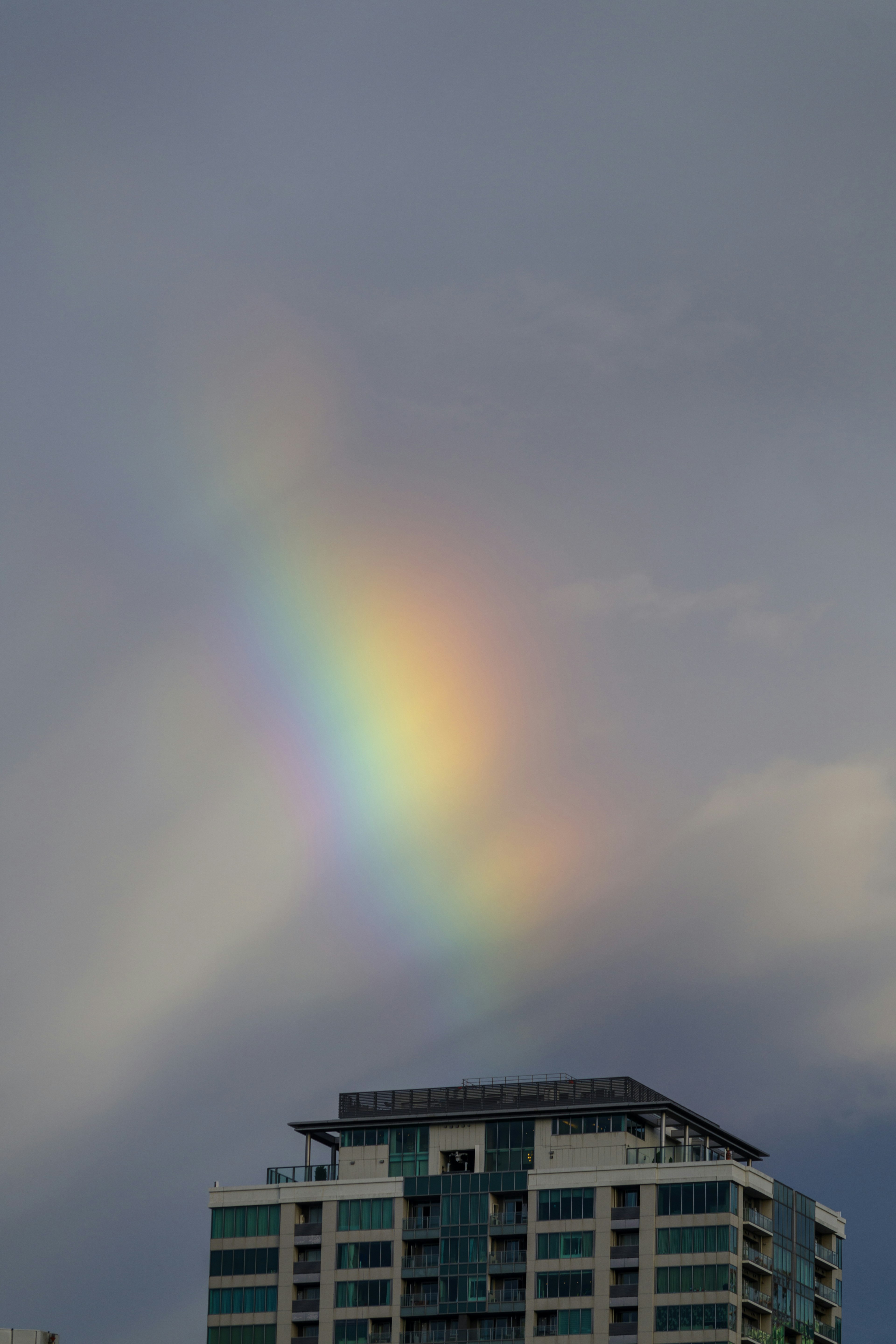 A rainbow appearing above a tall building under a cloudy sky