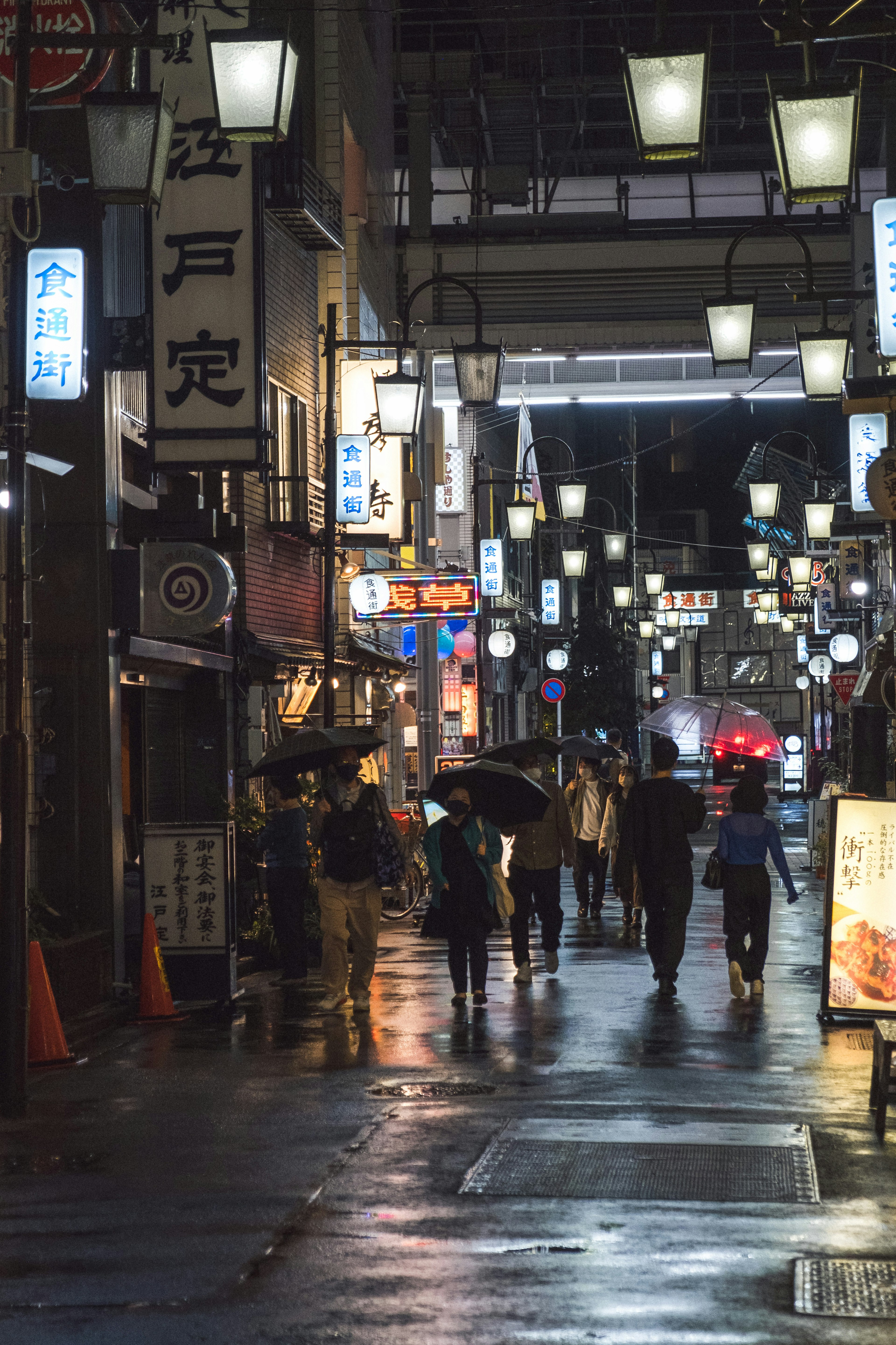 雨に濡れた夜の街並み、傘を持つ人々、明かりが灯った看板