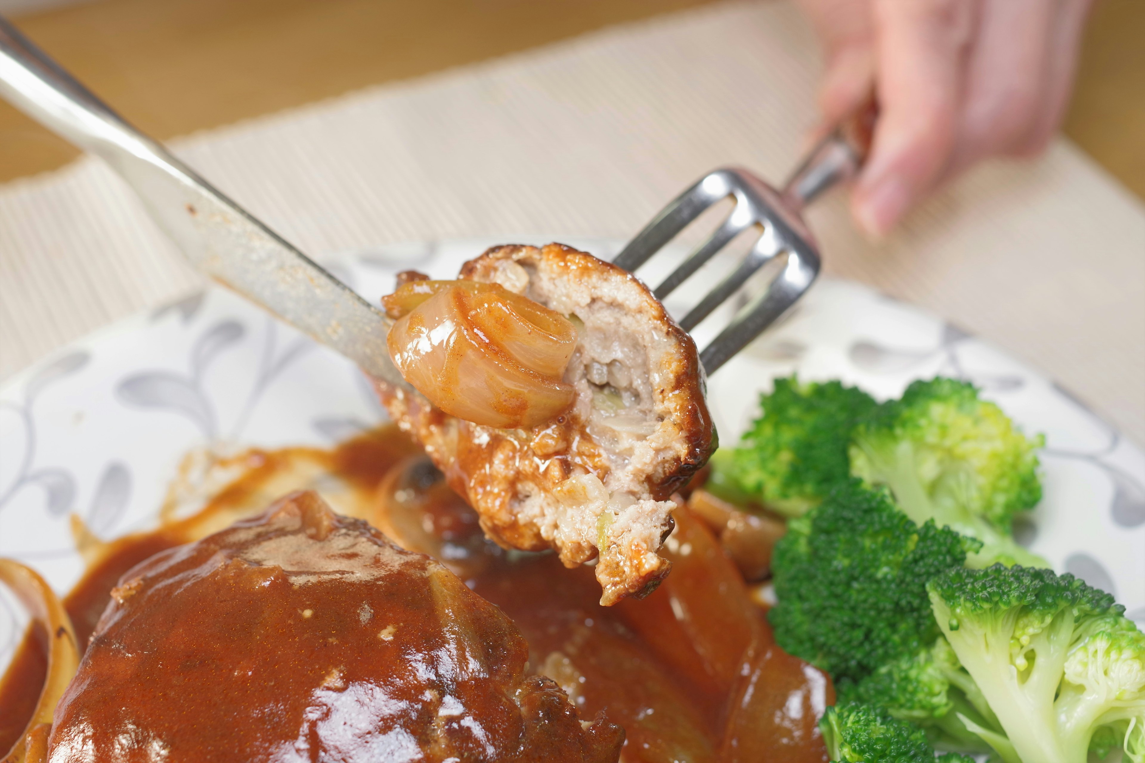 A fork holding a piece of hamburger steak with broccoli on the side