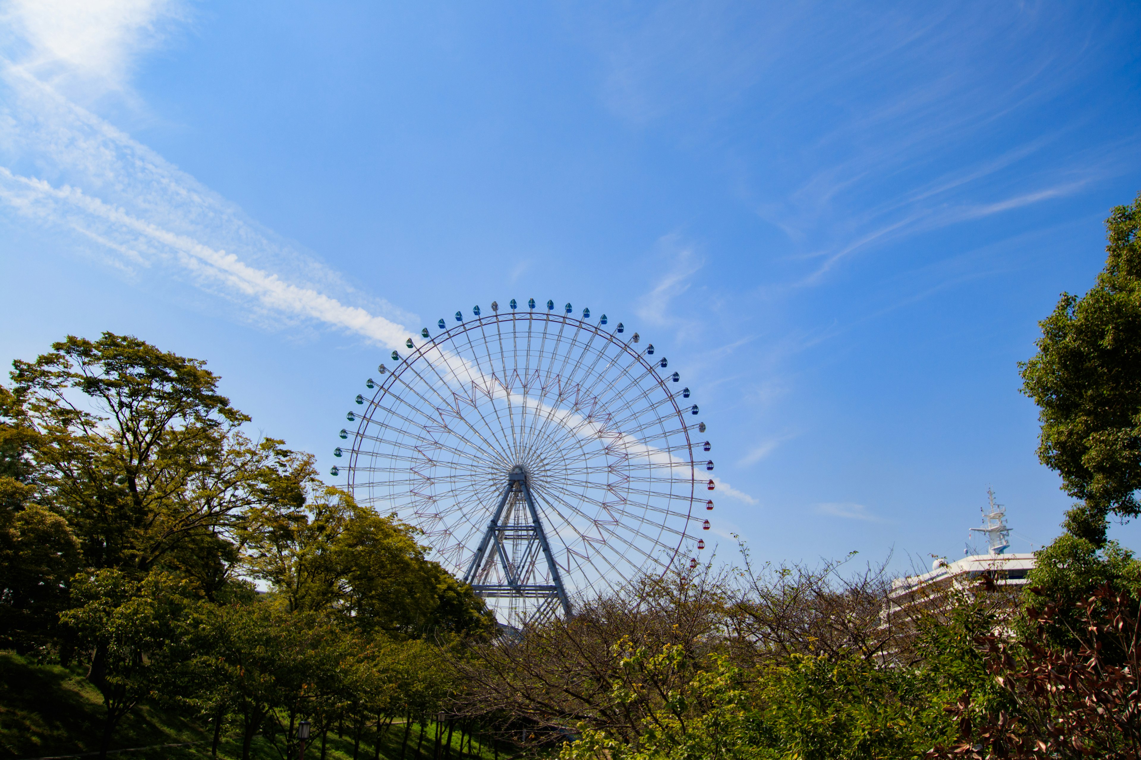 Riesenrad unter einem klaren blauen Himmel umgeben von grünen Bäumen