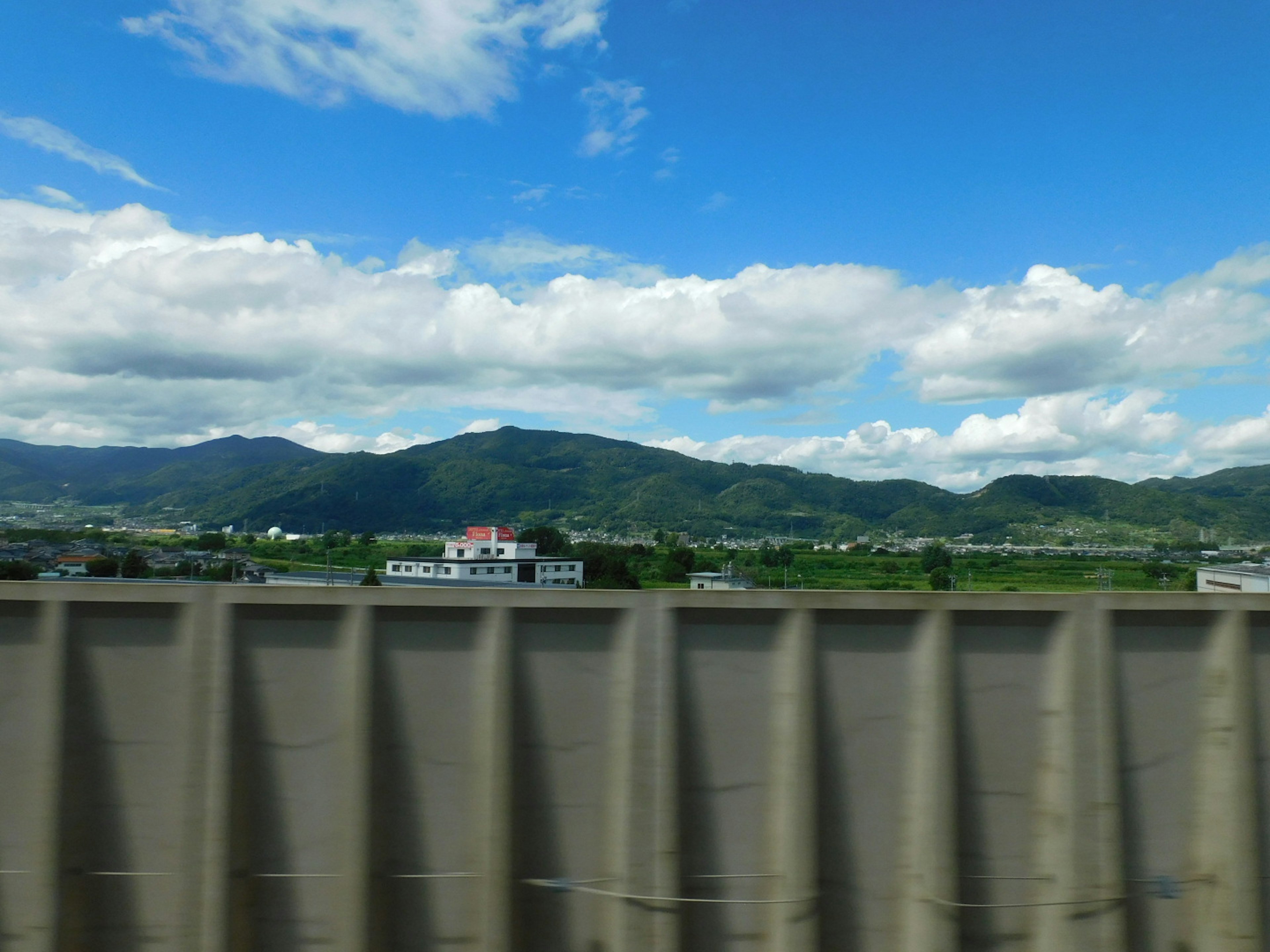 Landscape featuring green mountains under a blue sky with white clouds and a gray wall in the foreground