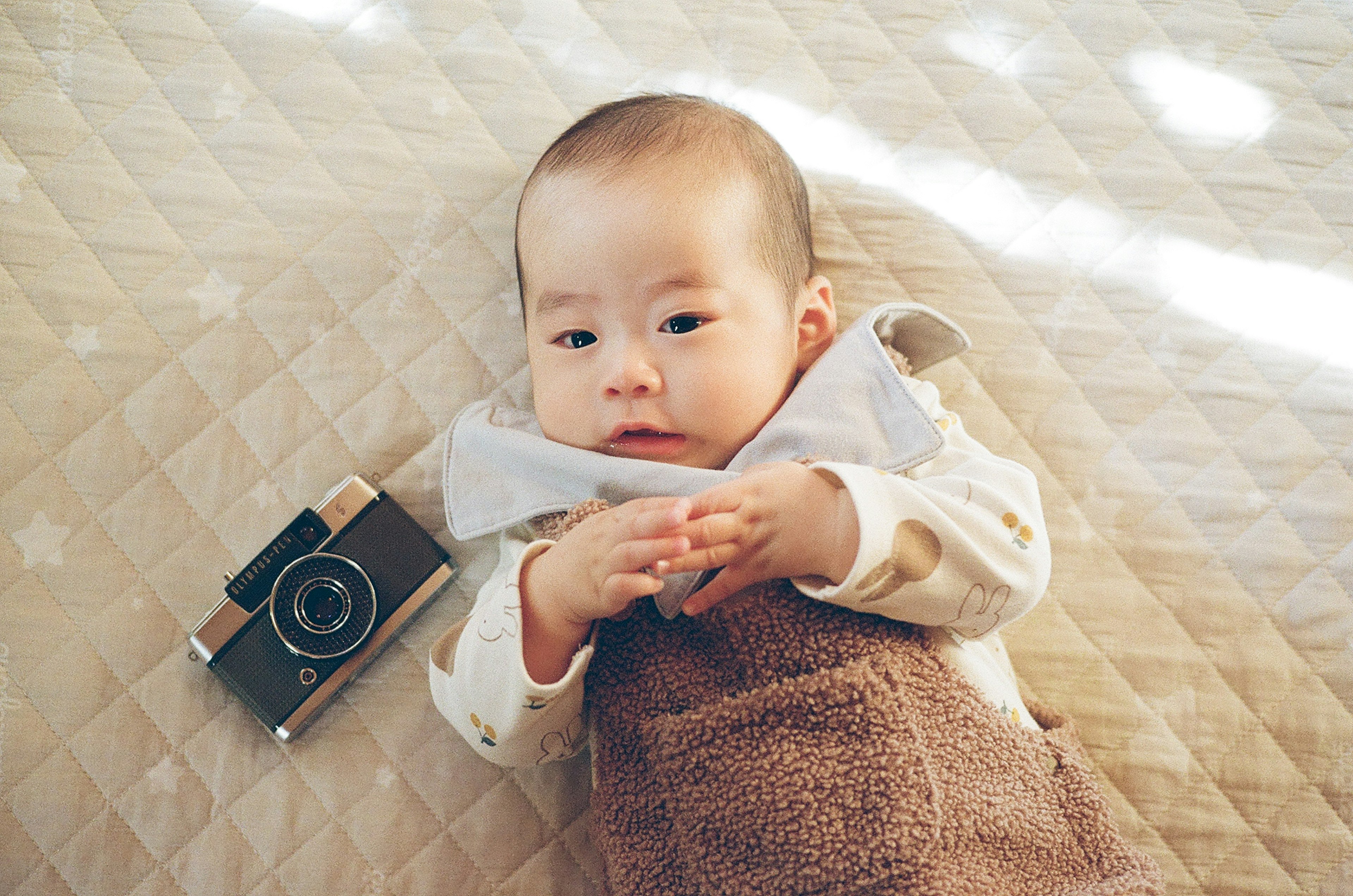 Baby lying beside a vintage camera on a quilted blanket