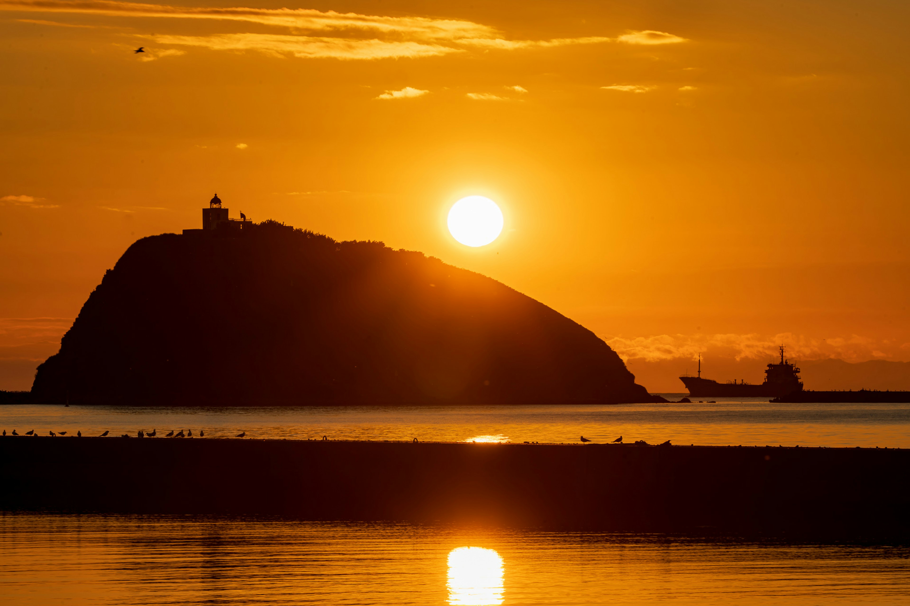 夕日が沈む中での島と灯台のシルエット