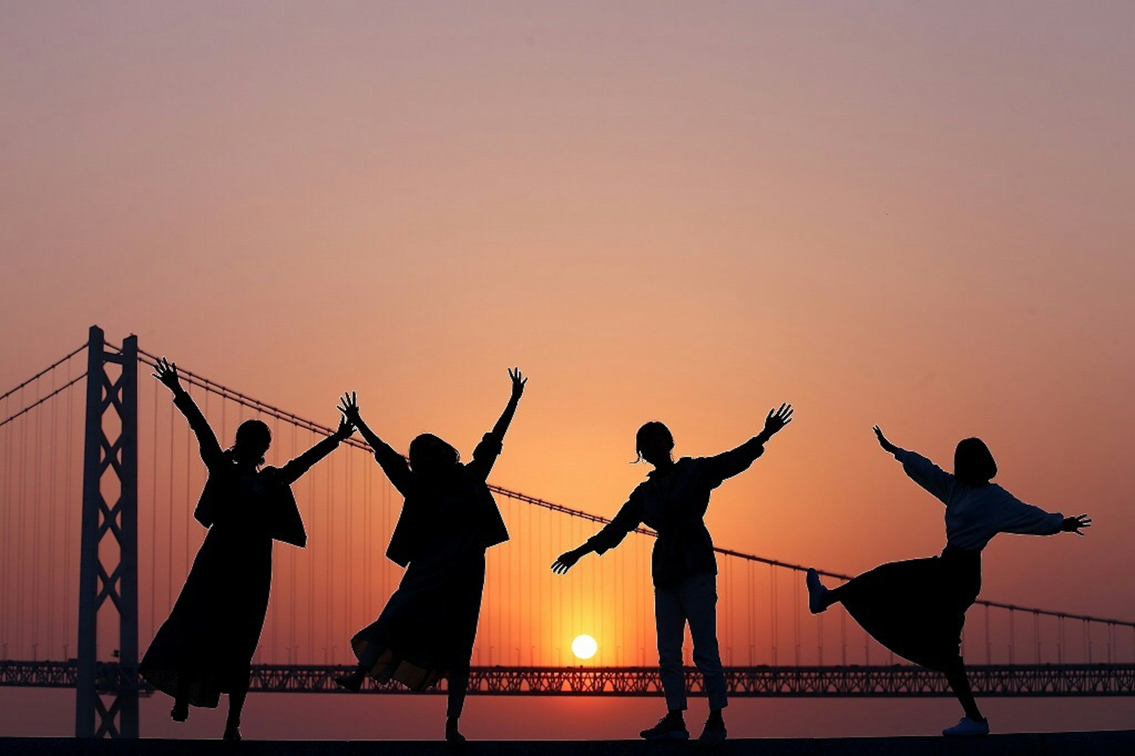 Silhouette de quatre personnes agitant la main contre un coucher de soleil avec un pont