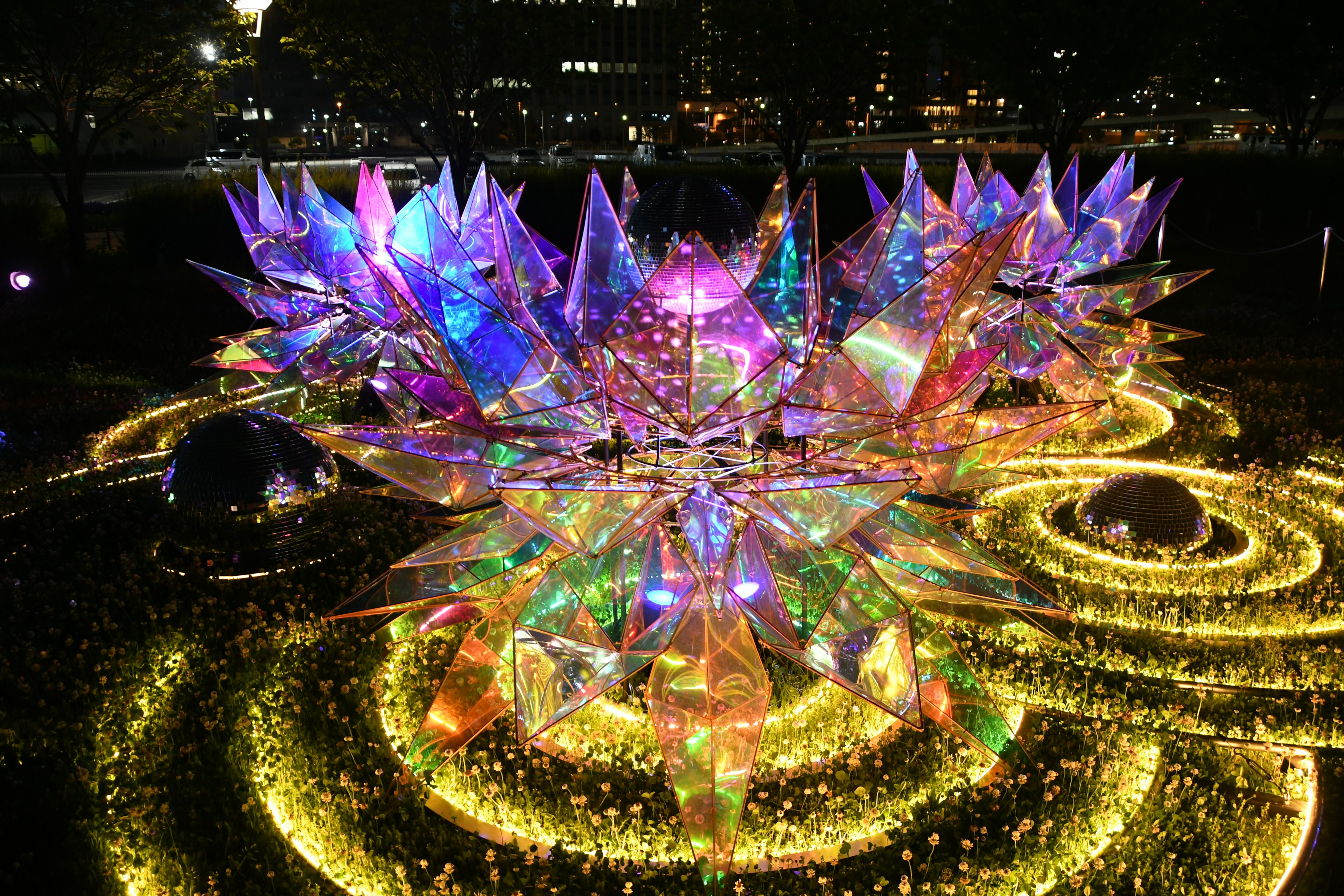 Eine große blumenähnliche Installation mit bunten Lichtern in einem Nachtpark