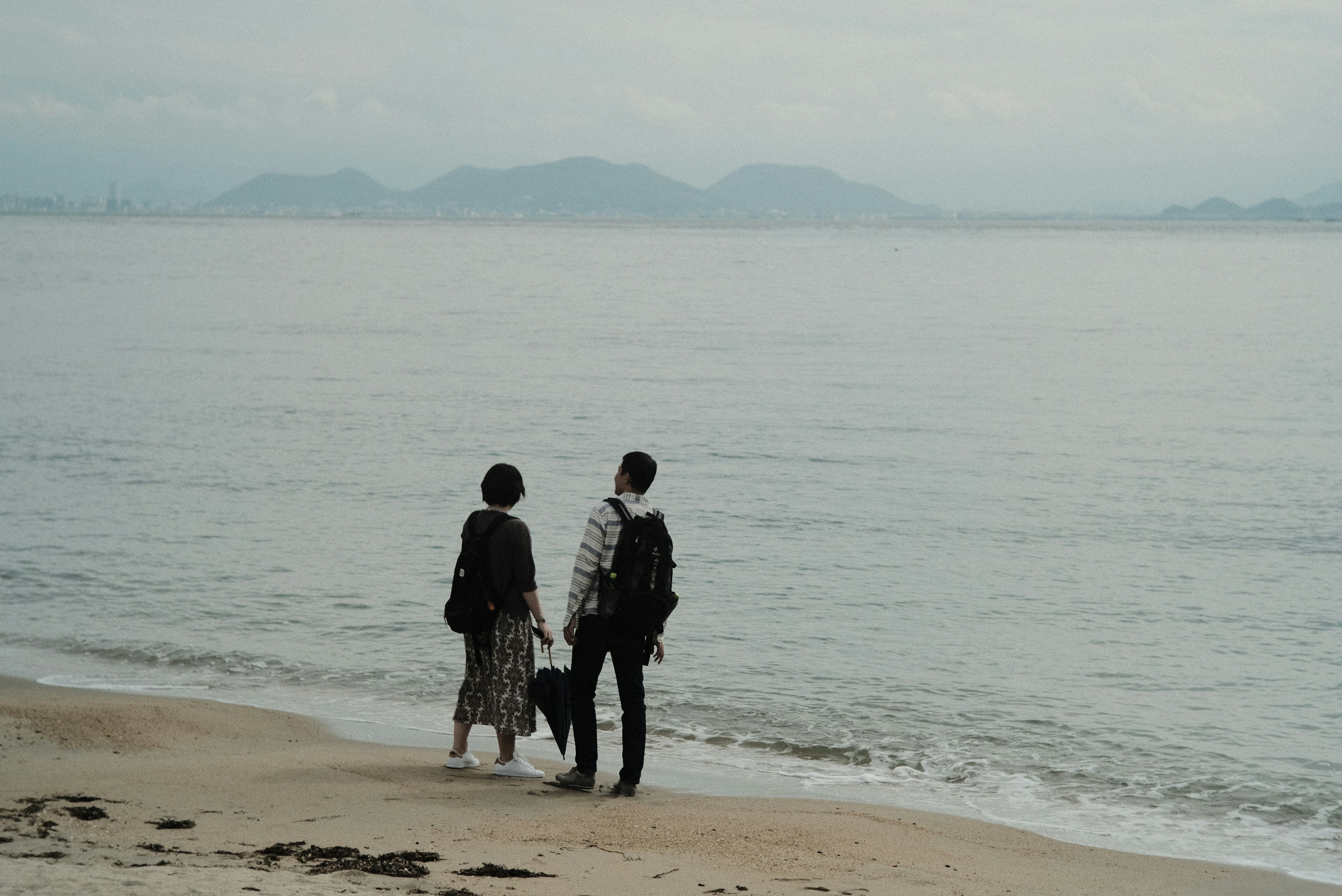 Dos personas de pie en la playa mirando al mar tranquilo