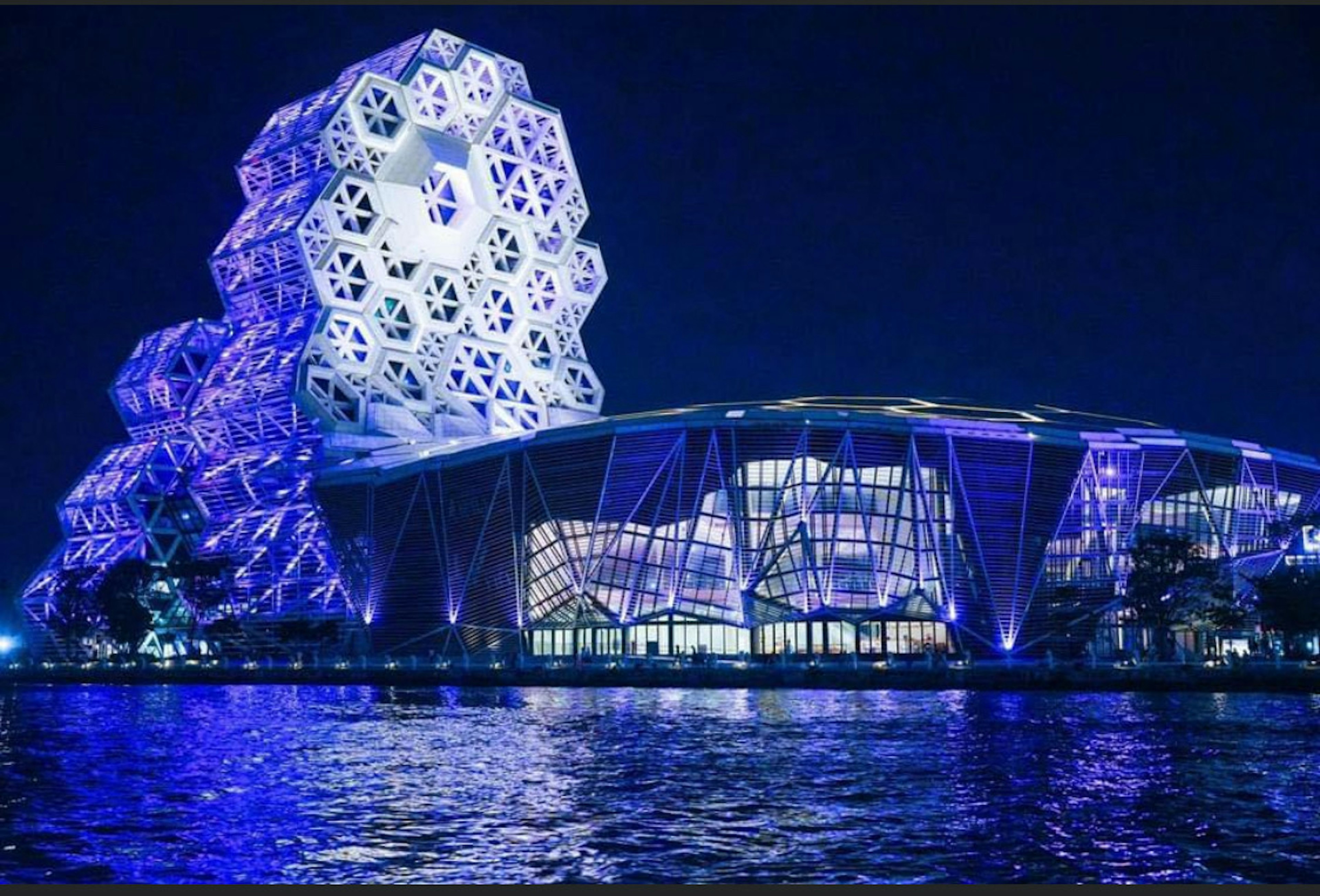 Bâtiment futuriste au bord de l'eau illuminé par une lumière bleue avec un design unique