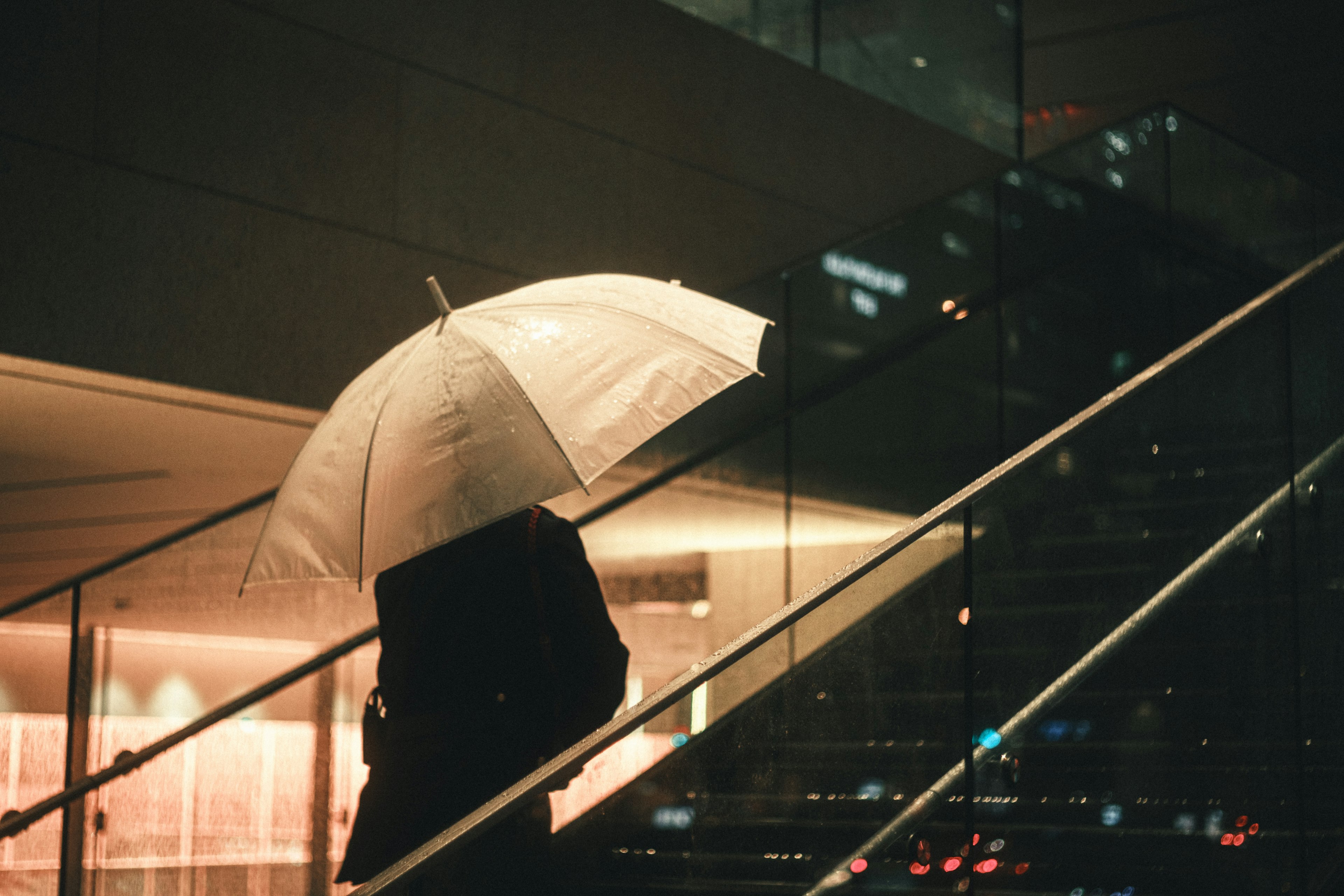 Eine Person mit einem Regenschirm, die Treppen in einer nächtlichen Stadtlandschaft hinaufsteigt