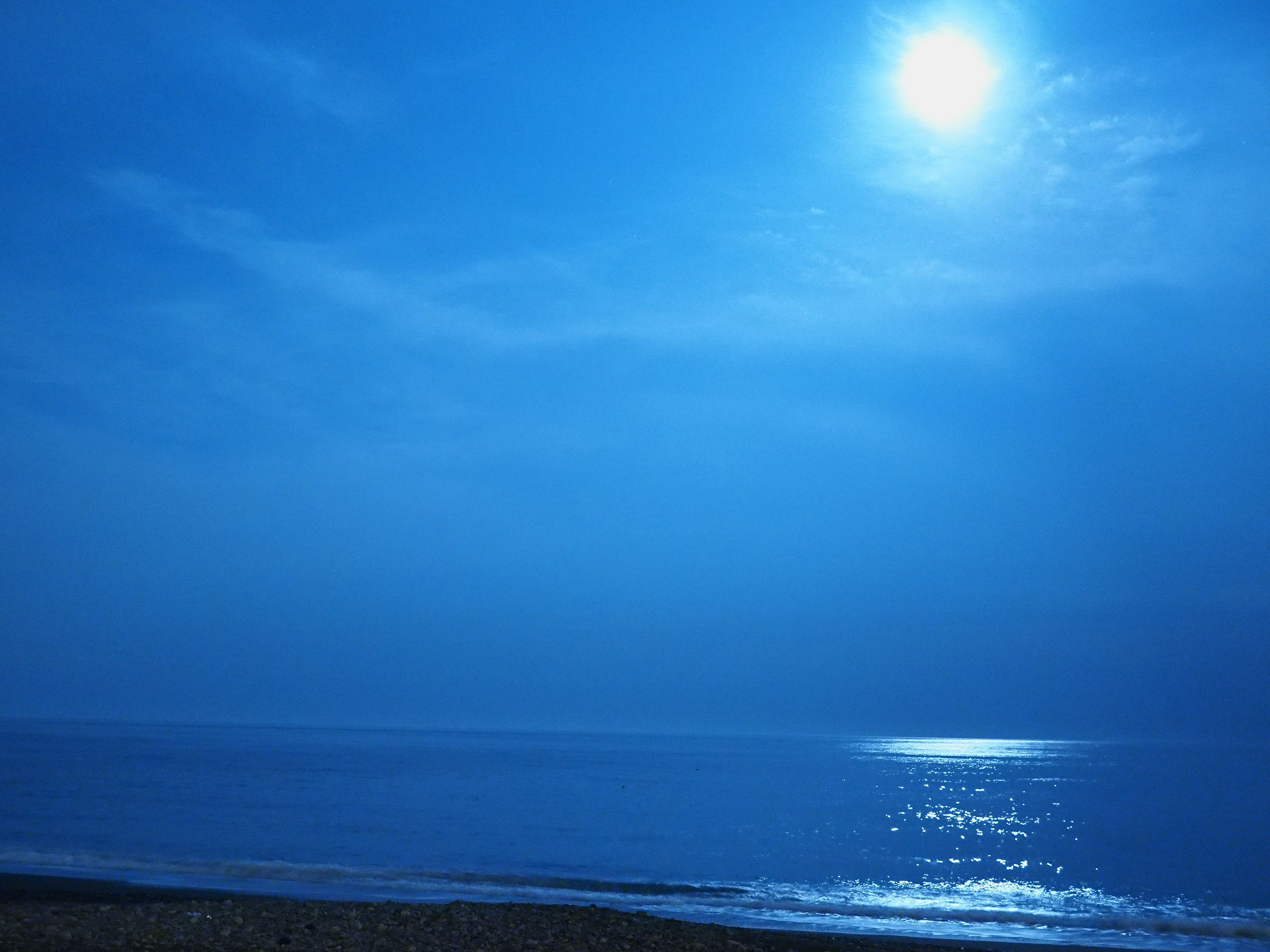 Escena nocturna tranquila con luna llena reflejándose en el mar azul y el cielo