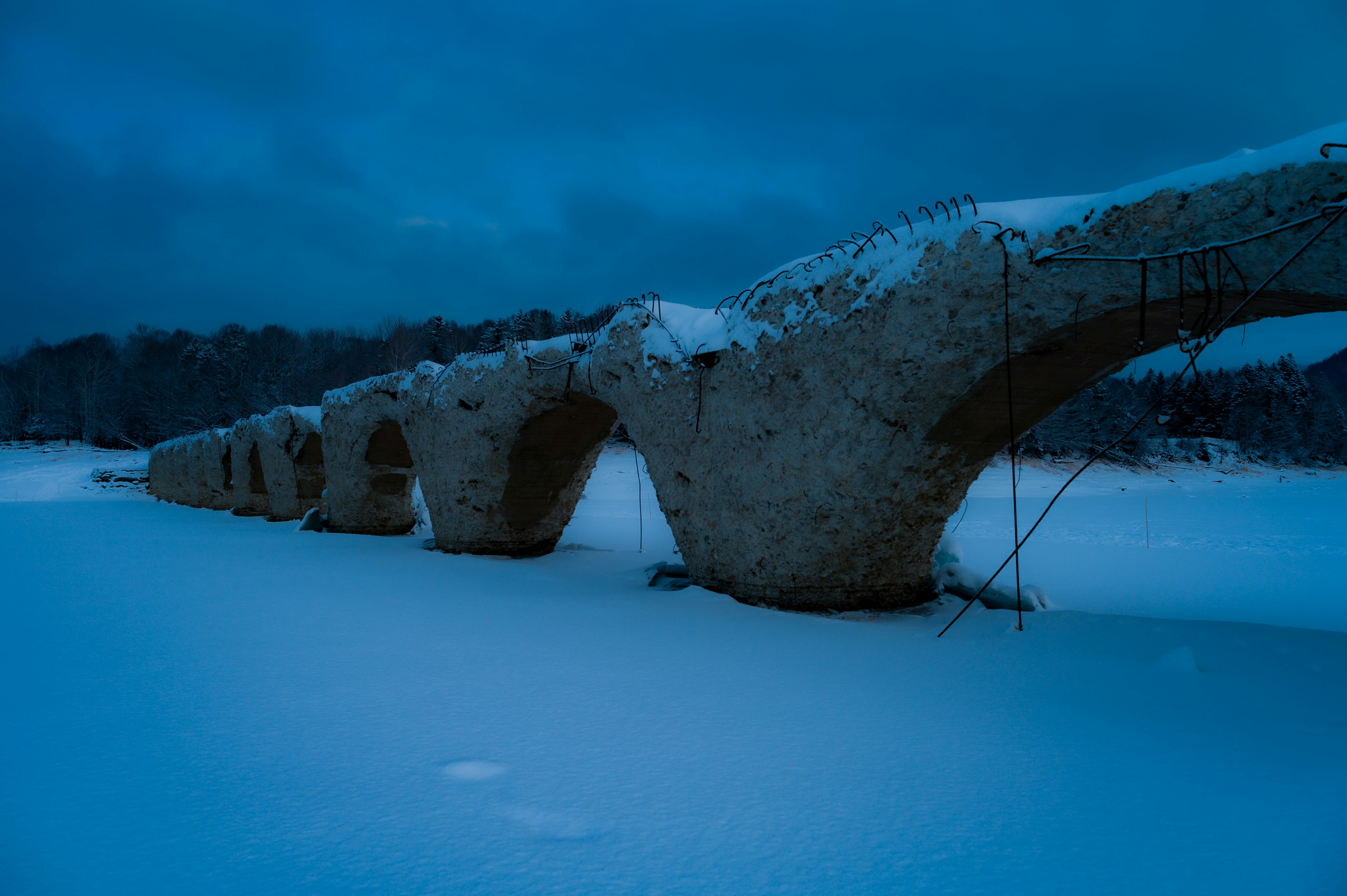 Ruinas de un puente cubierto de nieve que emergen en un paisaje de luz azul