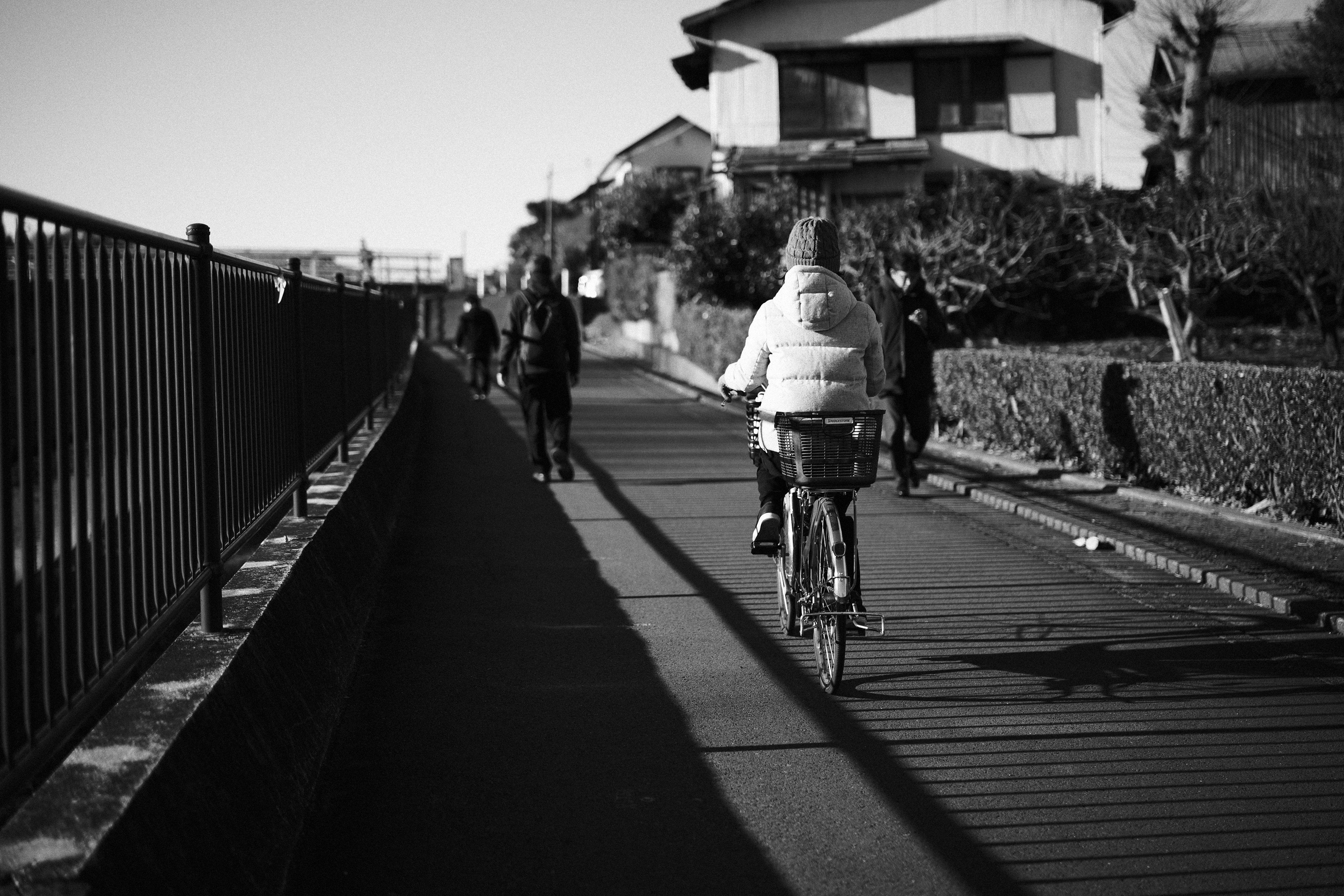 白黒の街道を自転車で走る人物と歩行者たちの風景