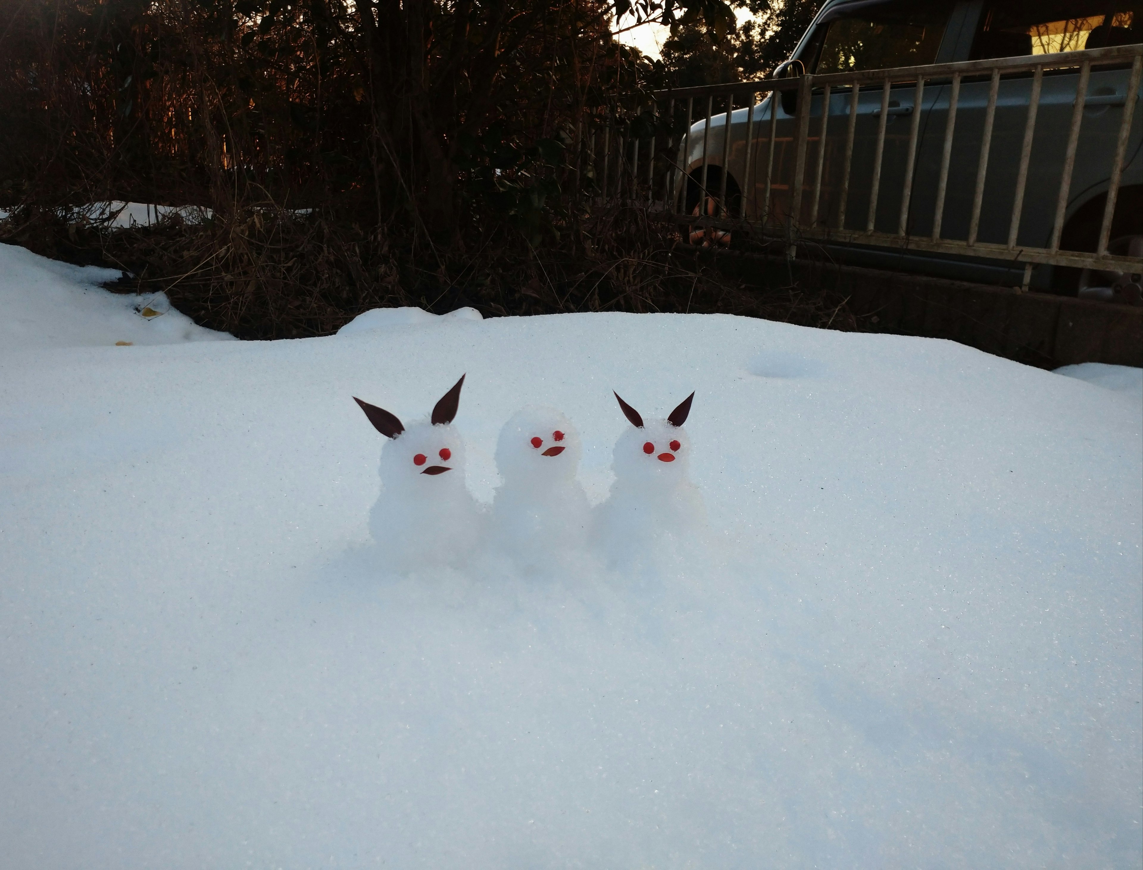 雪の中に立っている三匹のウサギの雪だるま白い雪と赤い目が特徴