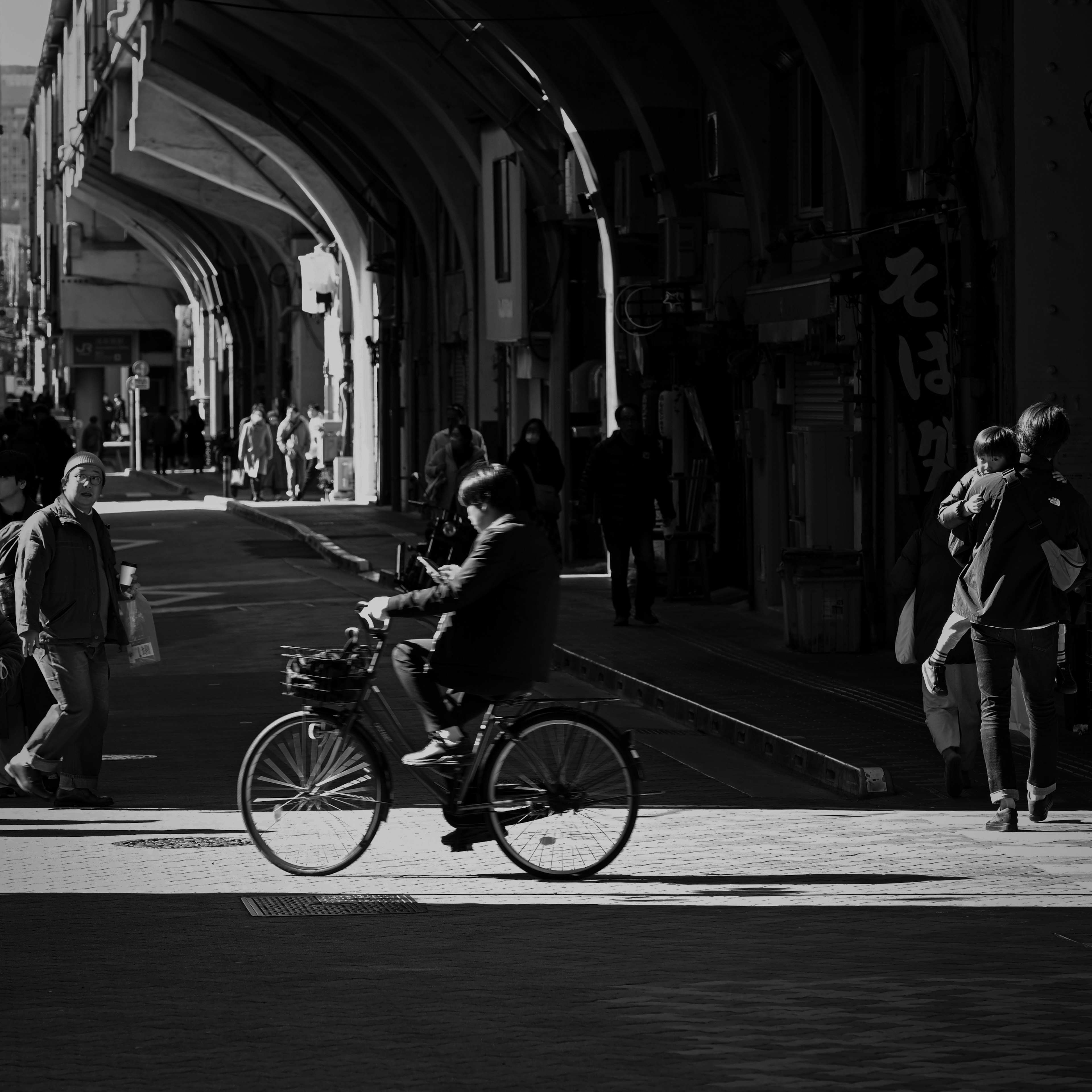 Black and white photo of a man riding a bicycle in a busy street with pedestrians