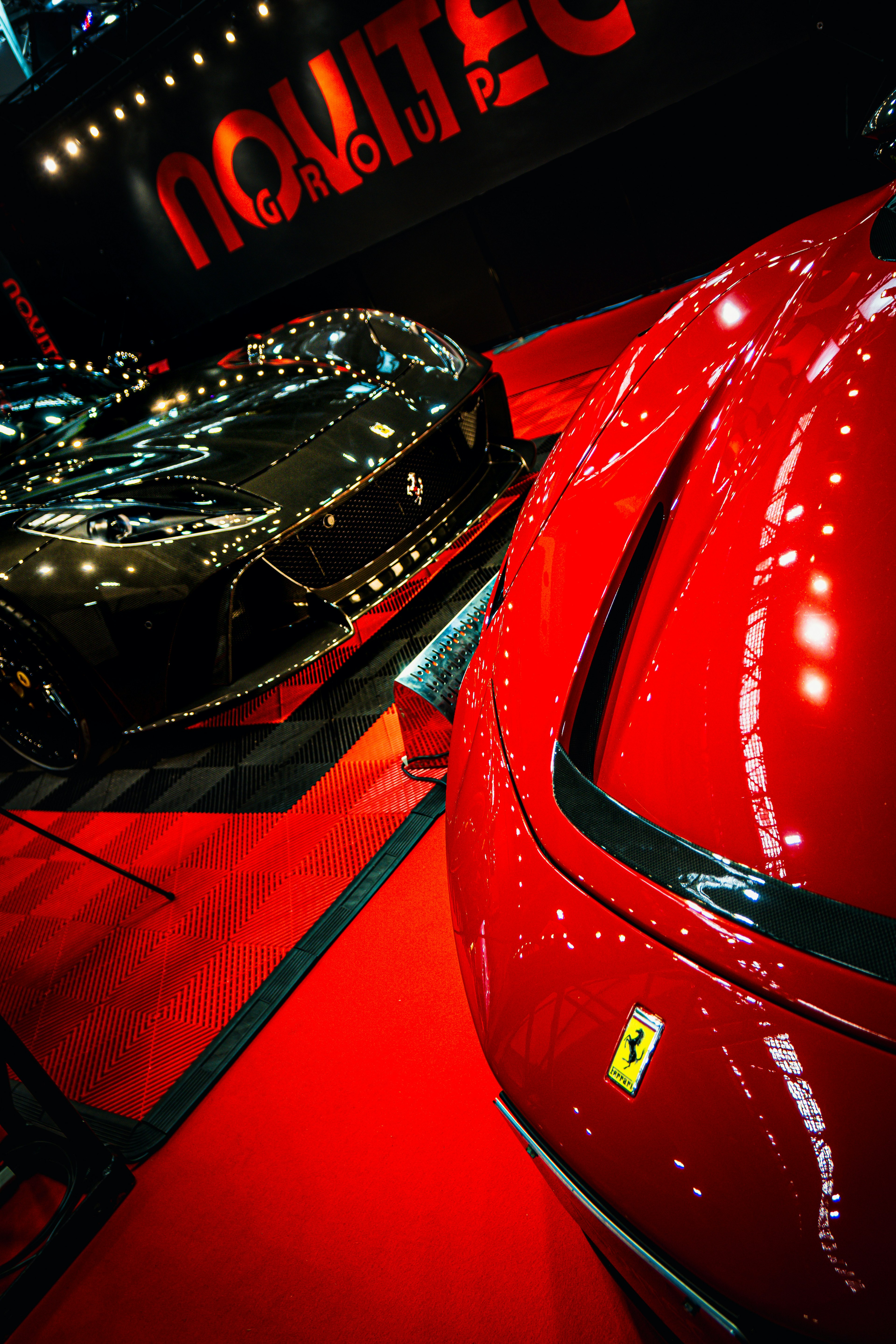 Ferrari rouge et voiture noire exposées à un salon automobile