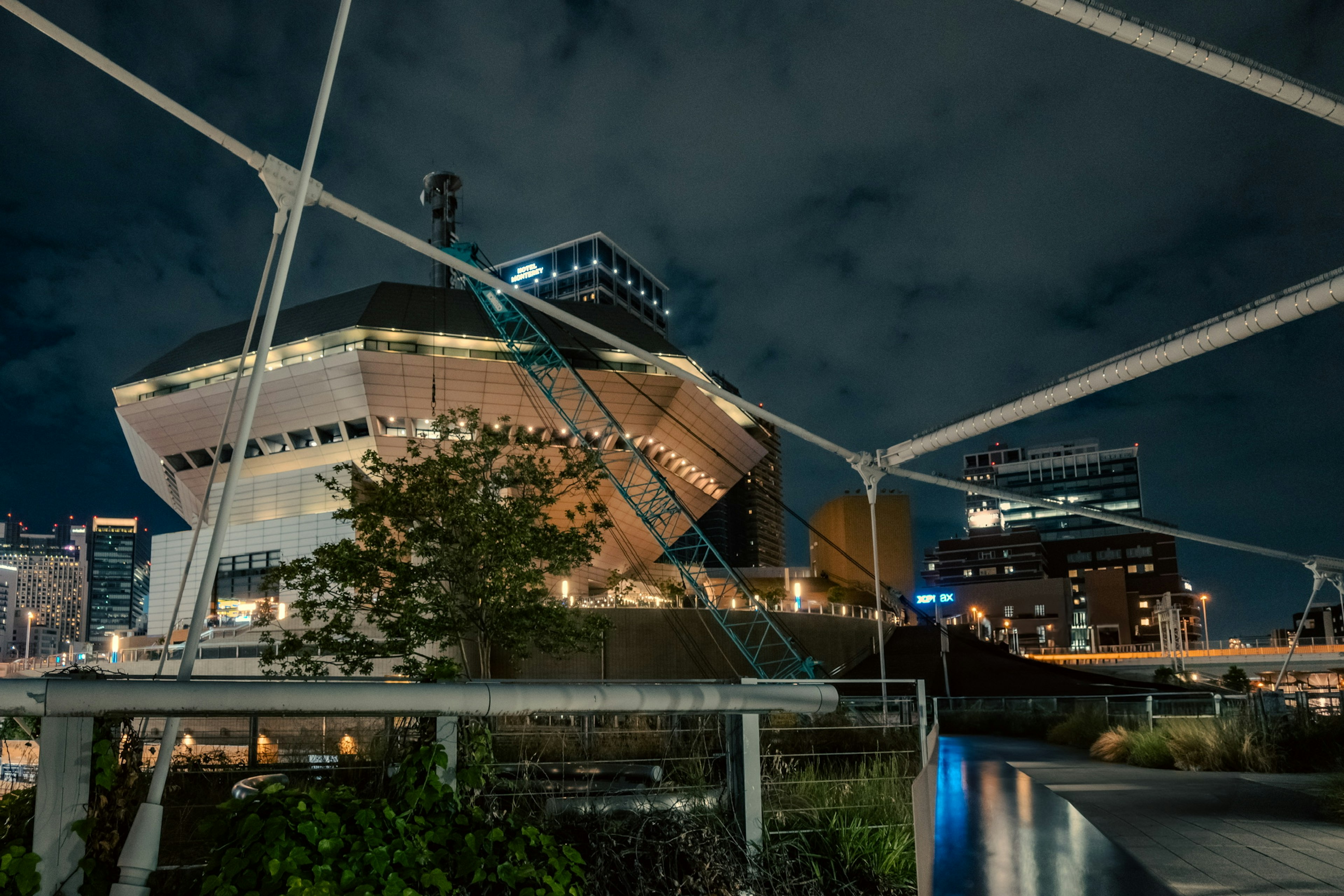 Estructura arquitectónica única iluminada por la noche rodeada de paisaje urbano y vegetación