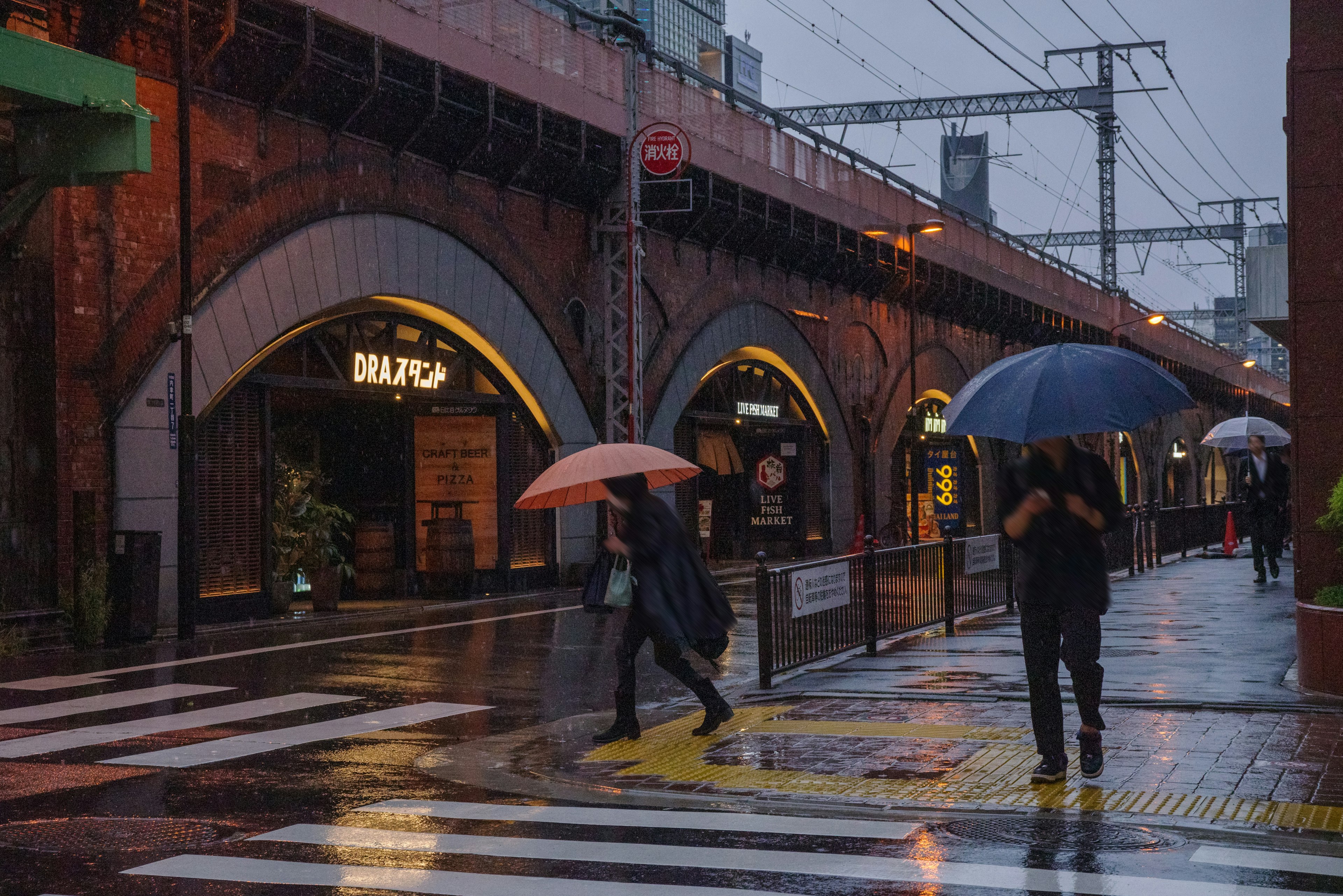 People with umbrellas walking in the rain near brick archways and storefronts