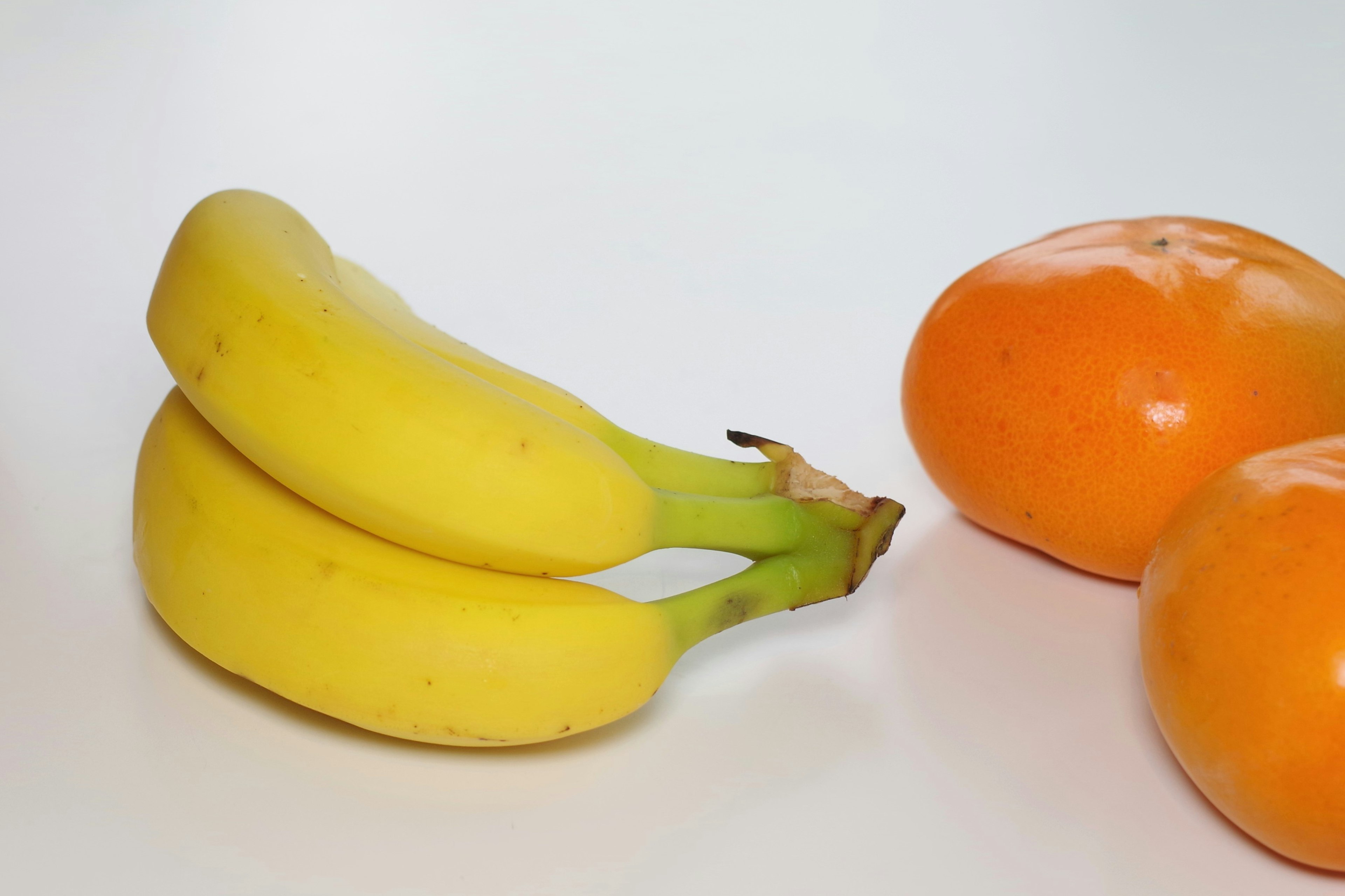 Due banane gialle e due frutti arancioni su uno sfondo bianco