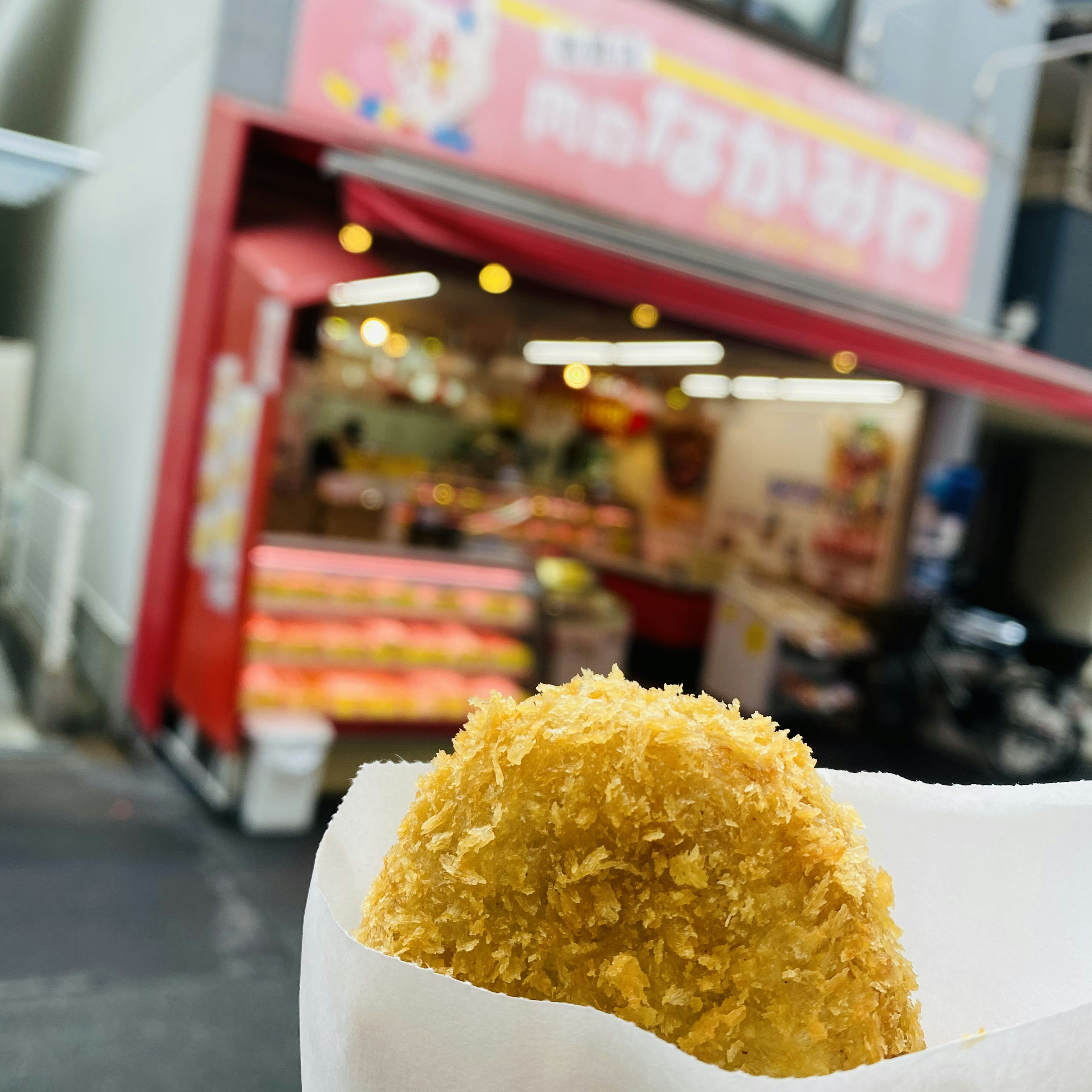 Un croquette doré au premier plan avec un stand de nourriture coloré en arrière-plan