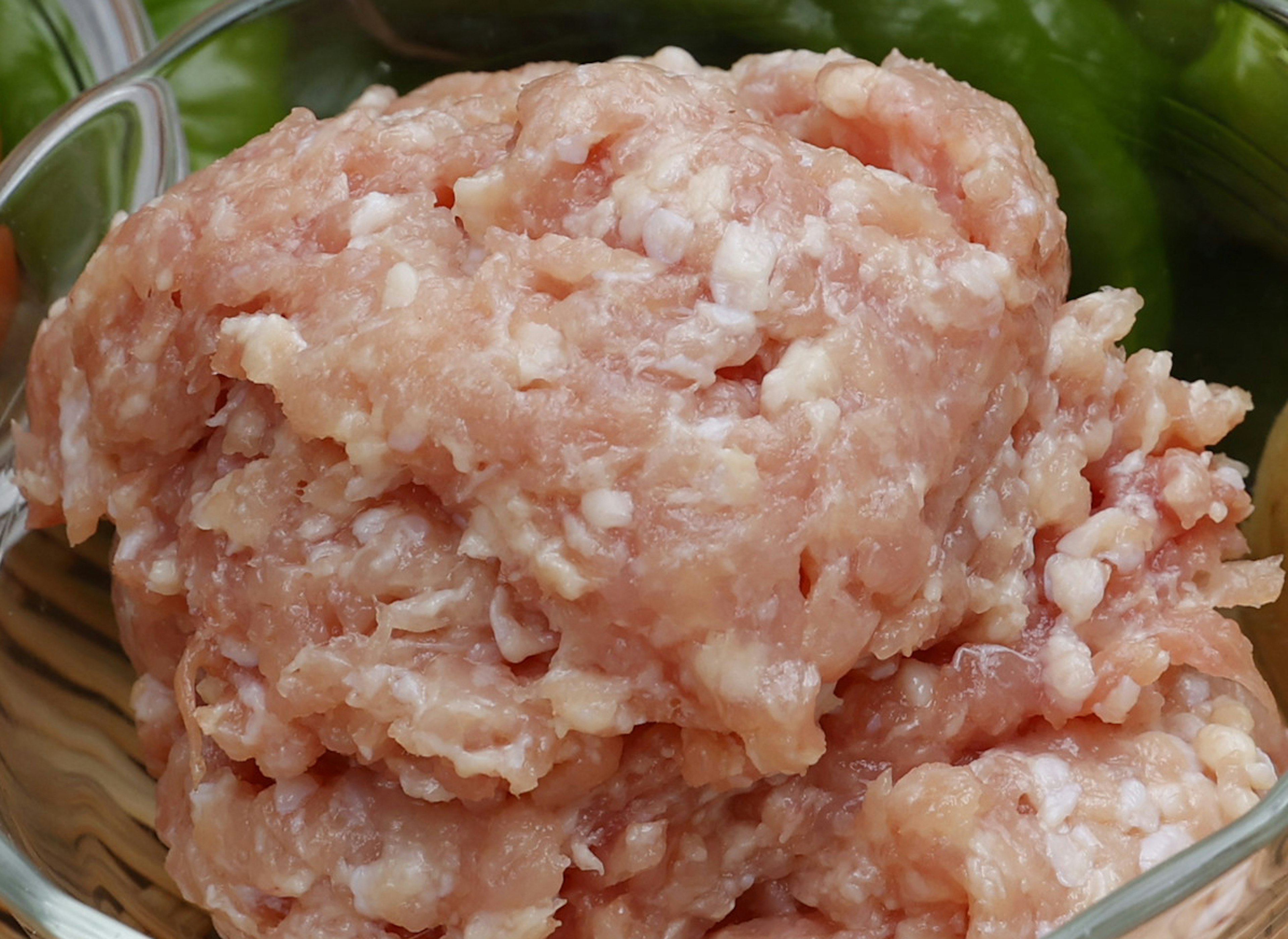 Ground meat in a glass bowl with green vegetables in the background