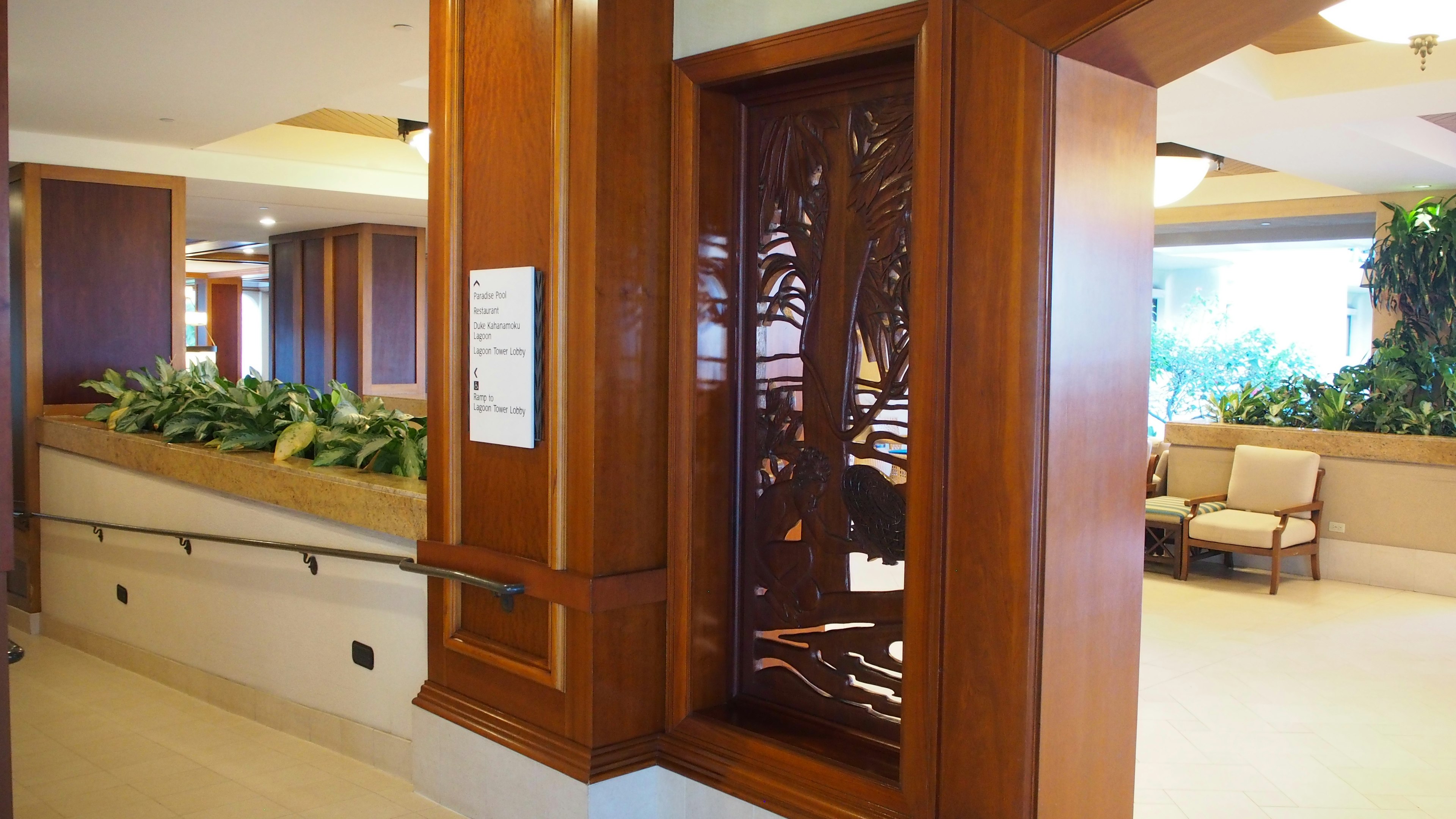 Bright lobby corner featuring a wooden decorative panel with intricate design and surrounding plants