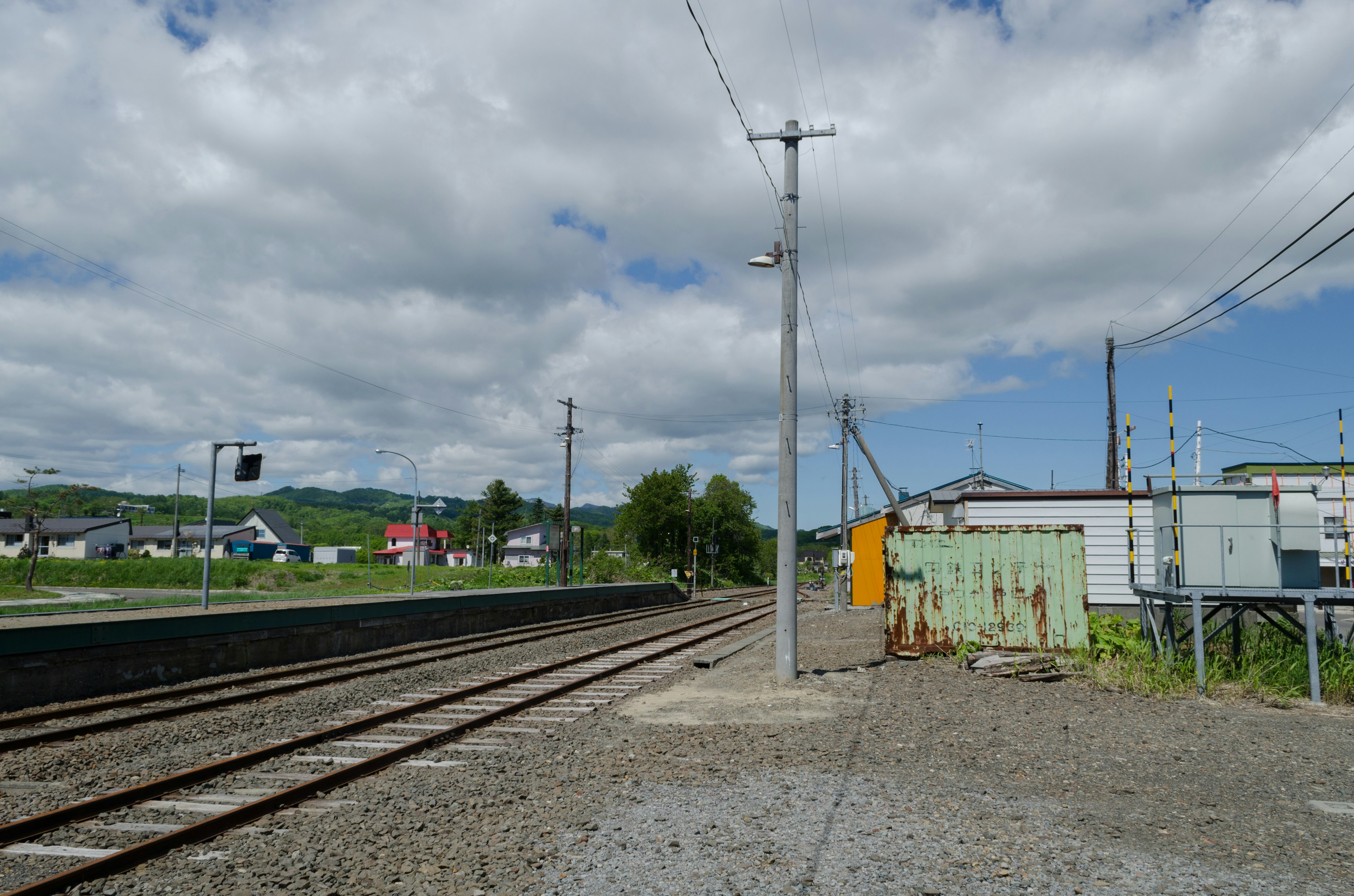 Paisaje a lo largo de la vía del tren con cielo azul y nubes blancas que presentan instalaciones de estación