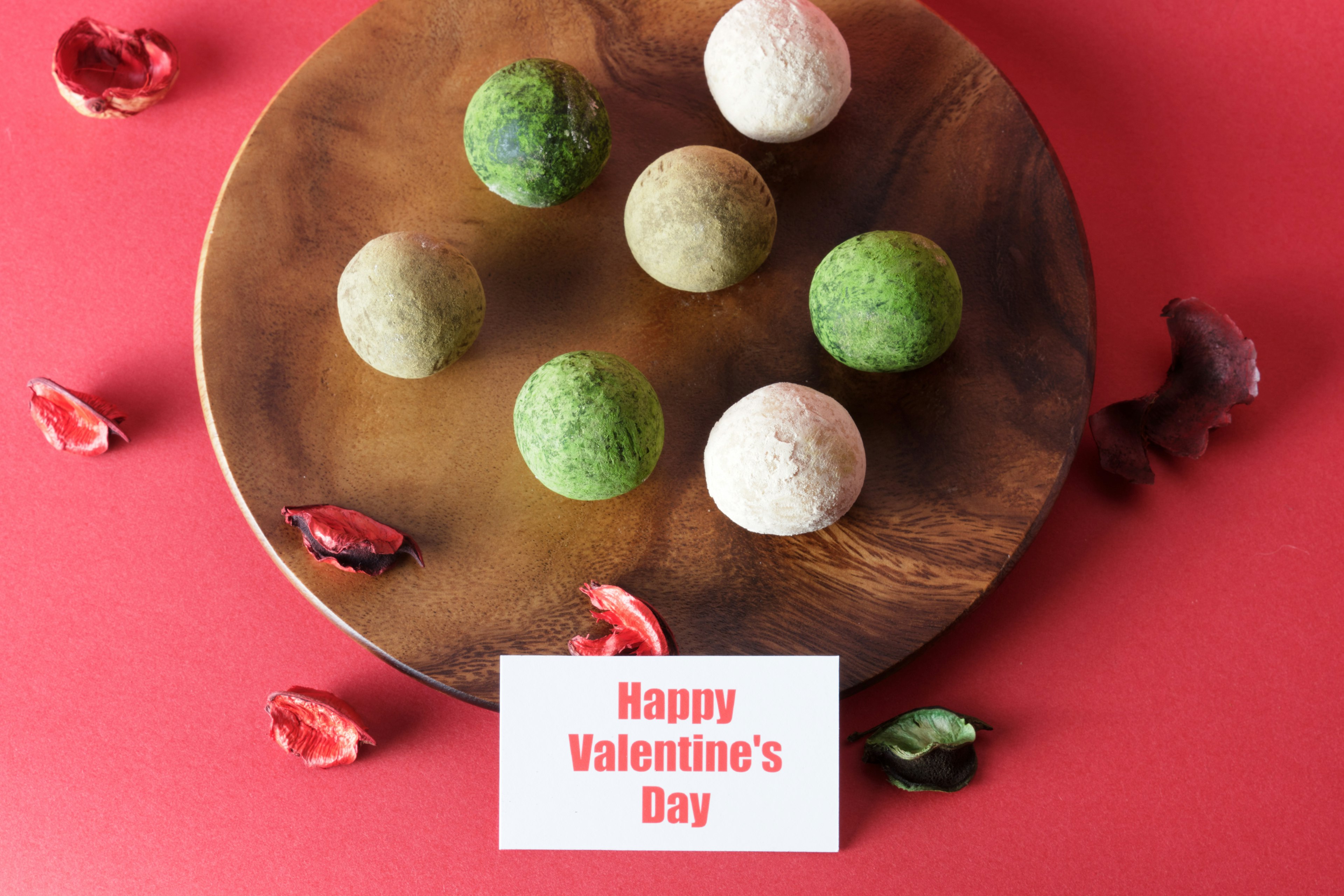 Image de boules vertes et blanches disposées sur une assiette en bois avec un fond rouge célébrant la Saint-Valentin