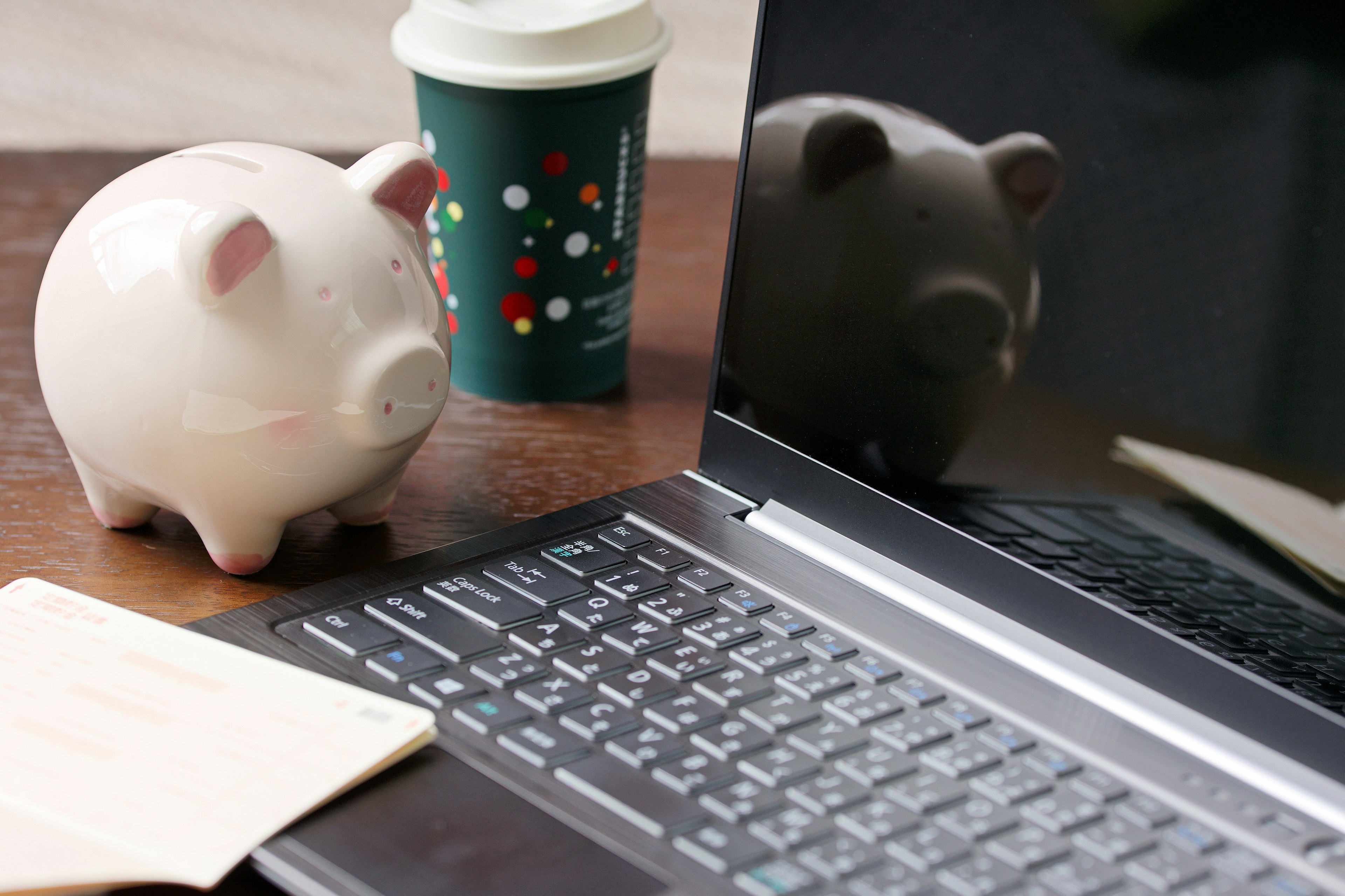 Un ordinateur portable sur un bureau avec une tirelire rose une tasse de café verte et un bloc-notes