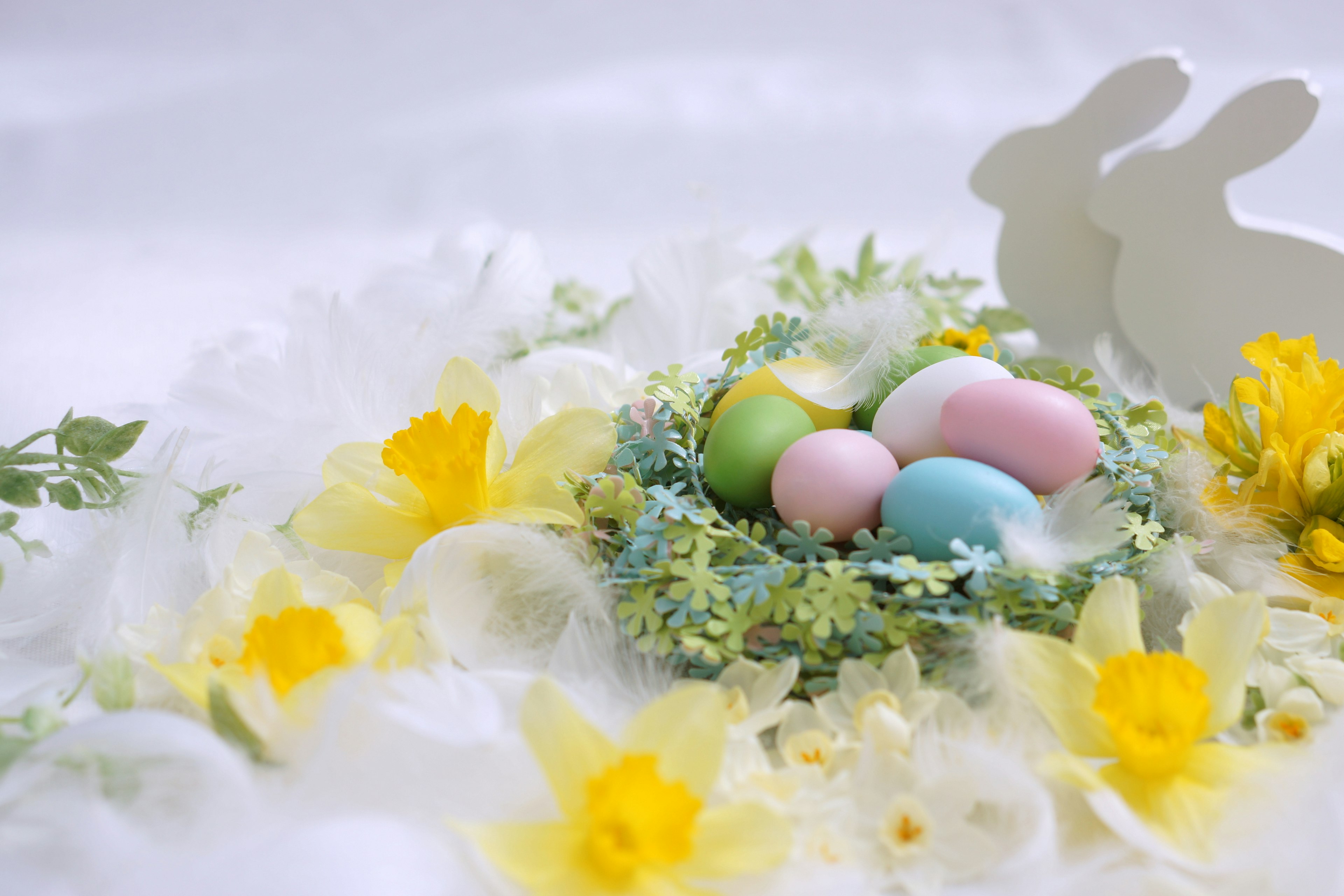 Bunte Eier in einem kleinen Nest mit gelben Blumen und weißen Hasen im Hintergrund