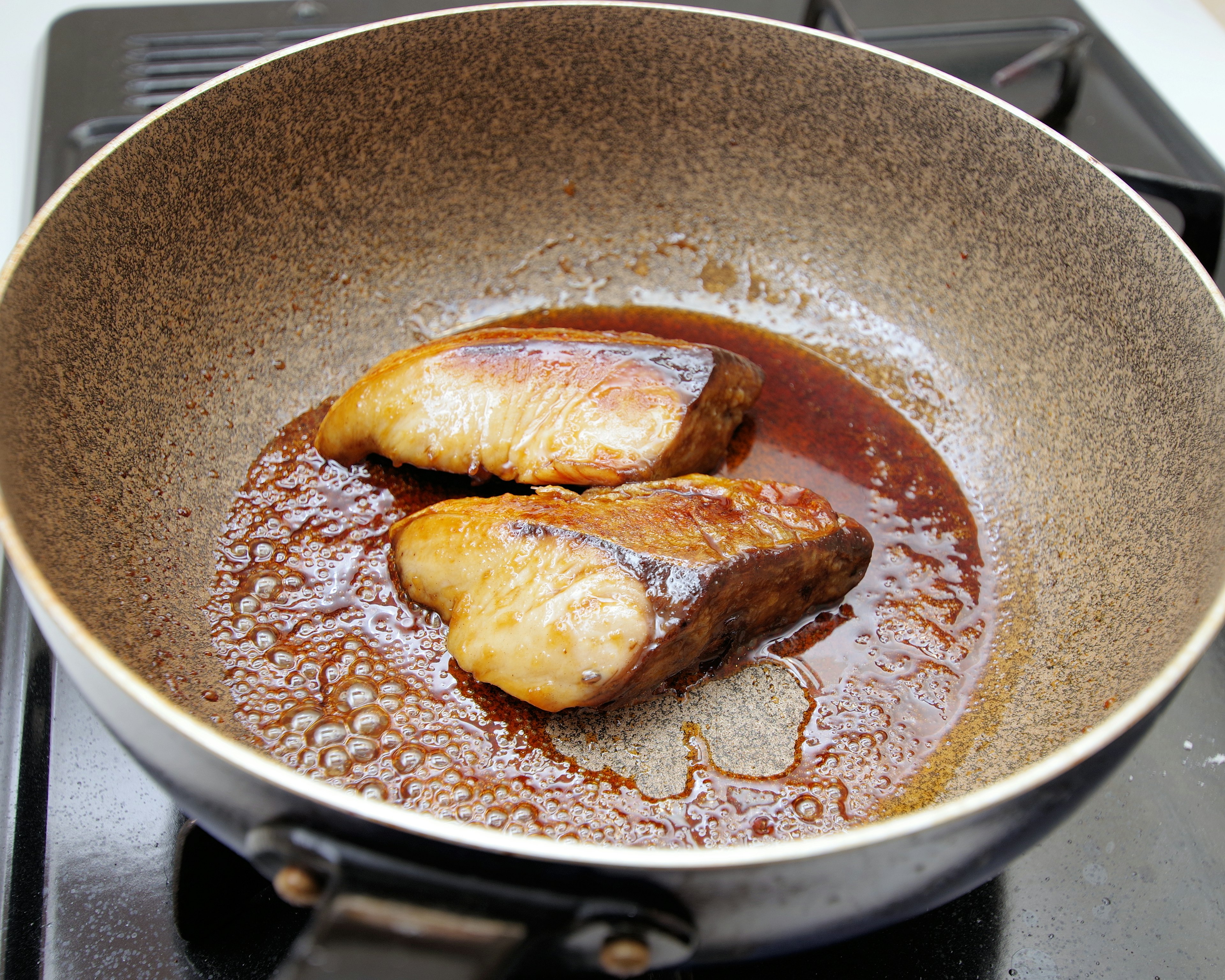 Dos filetes de pescado cocinándose en una sartén con una salsa rica