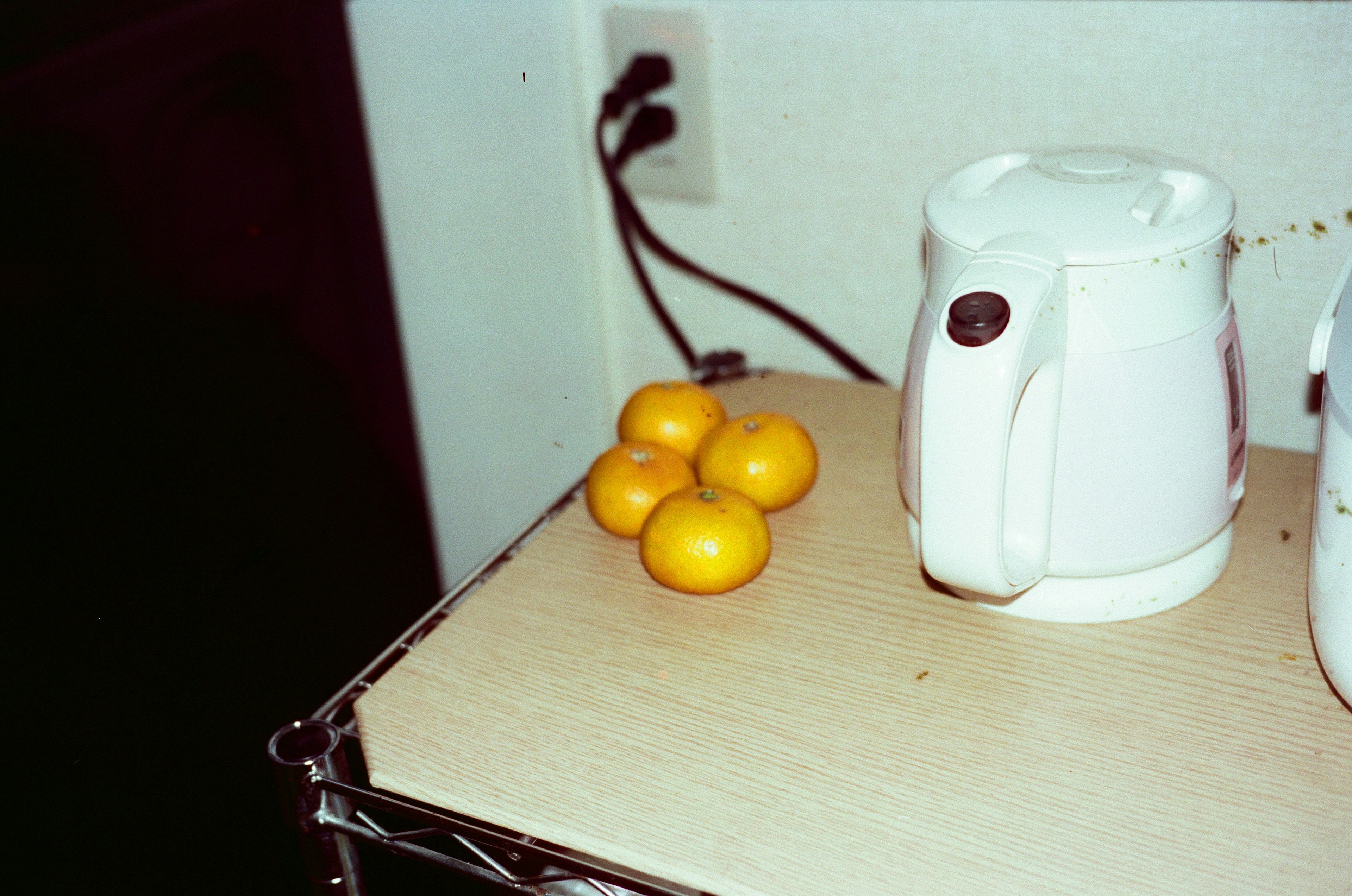 Hervidor eléctrico blanco junto a naranjas sobre una mesa de madera