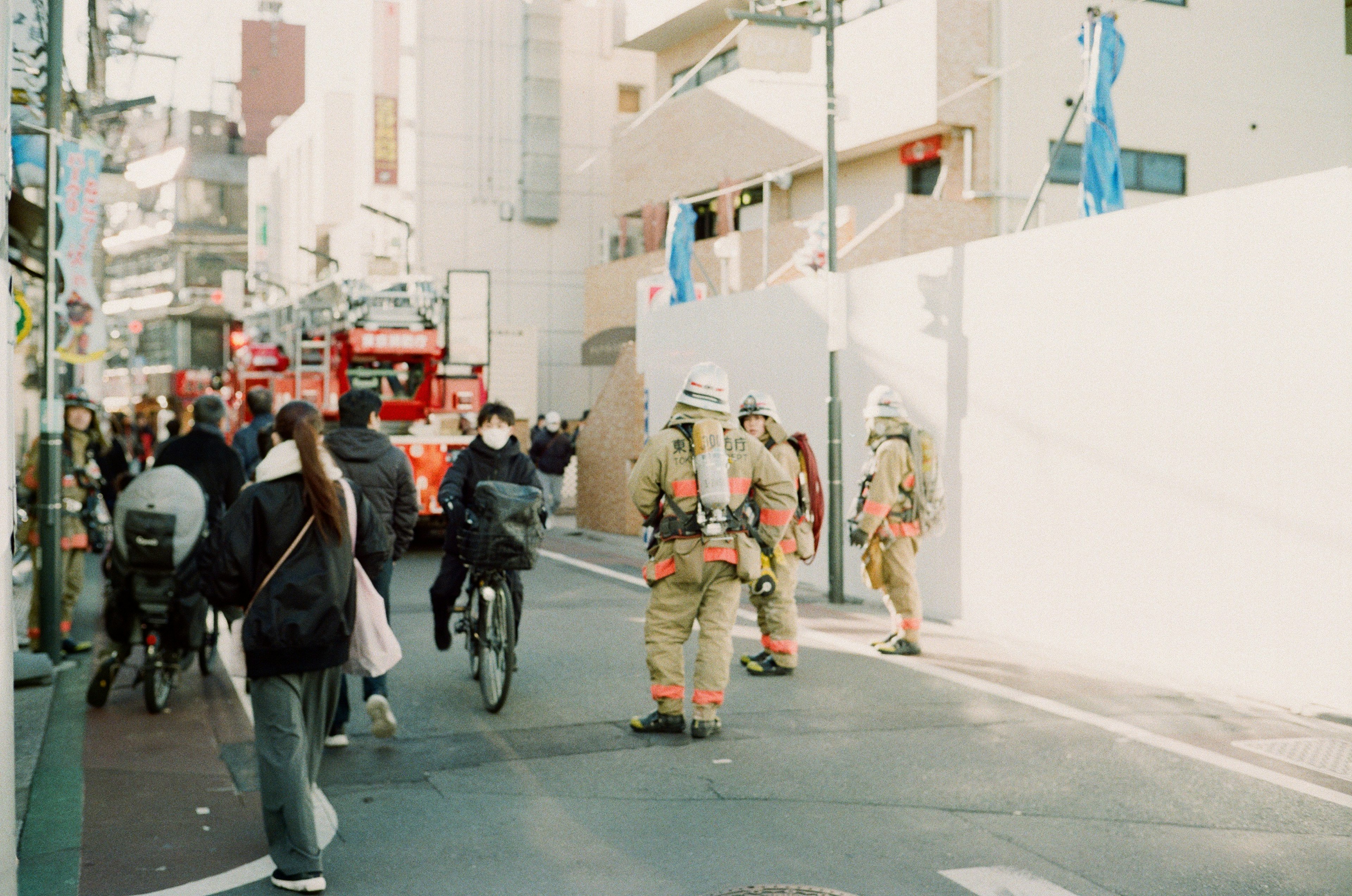 Firefighters in action on a city street with people on bicycles and a red fire truck