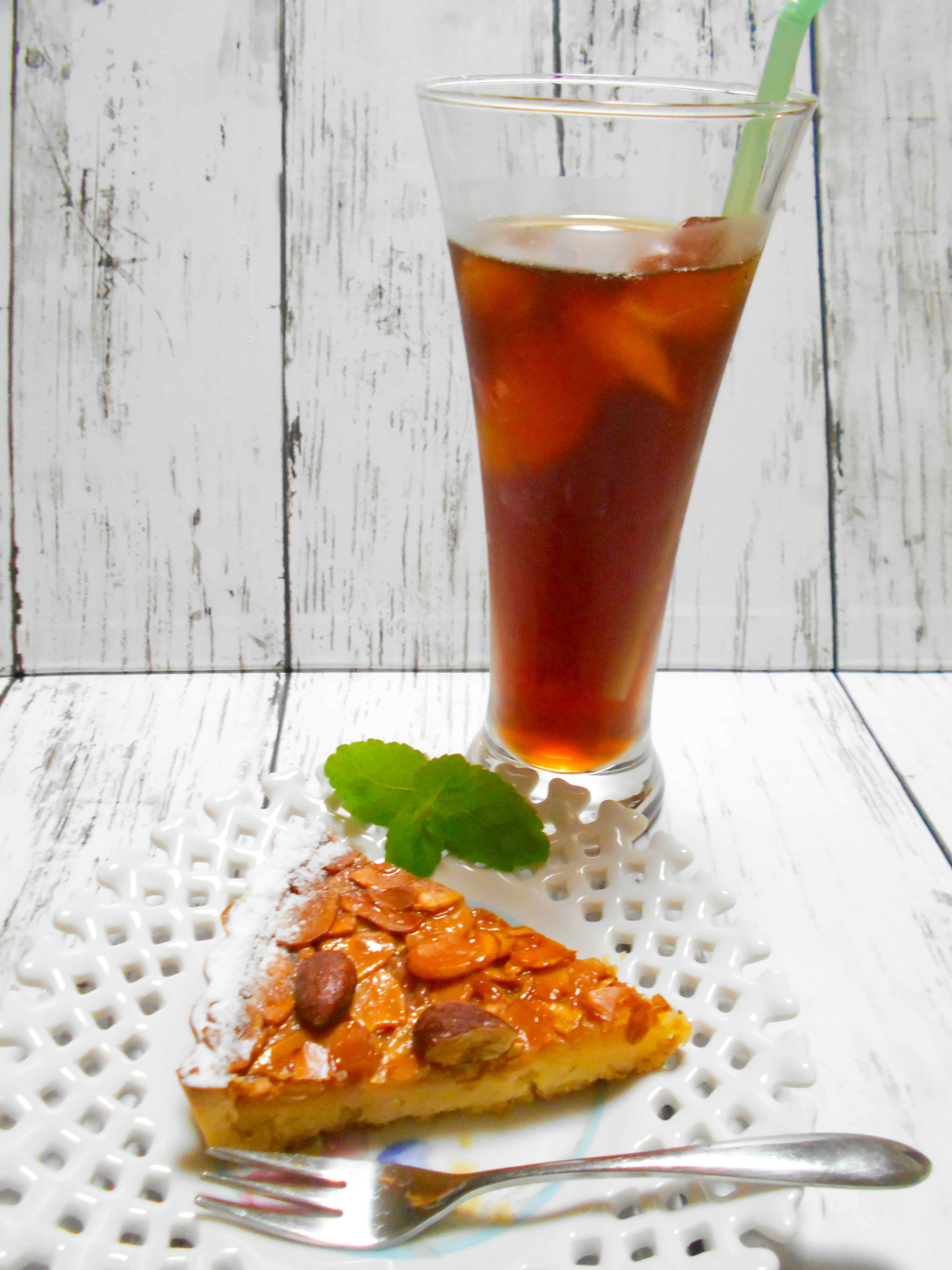 Part de gâteau aux amandes à côté d'un verre de thé glacé sur une table blanche