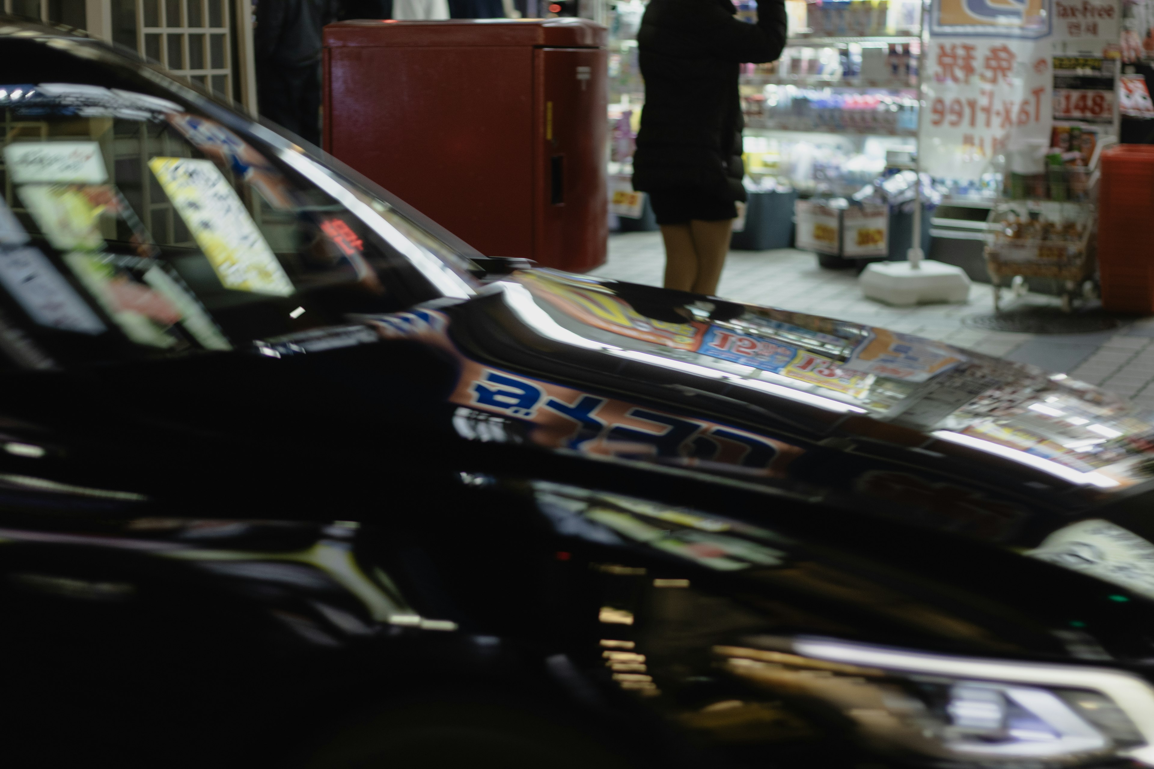 夜の街角で停車中の黒い車と背景の店舗