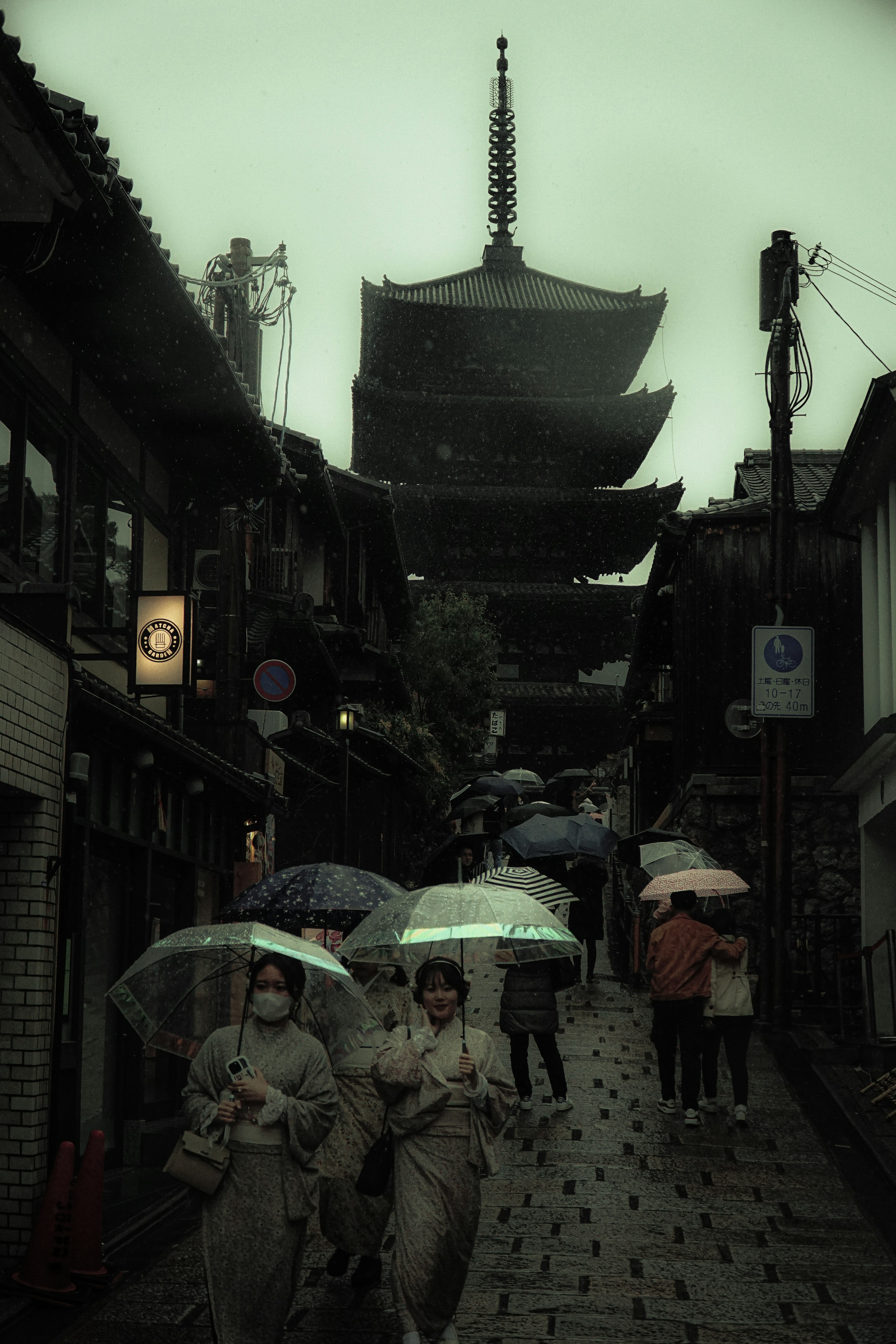 Personas caminando bajo la lluvia con paraguas cerca de una pagoda en una calle antigua