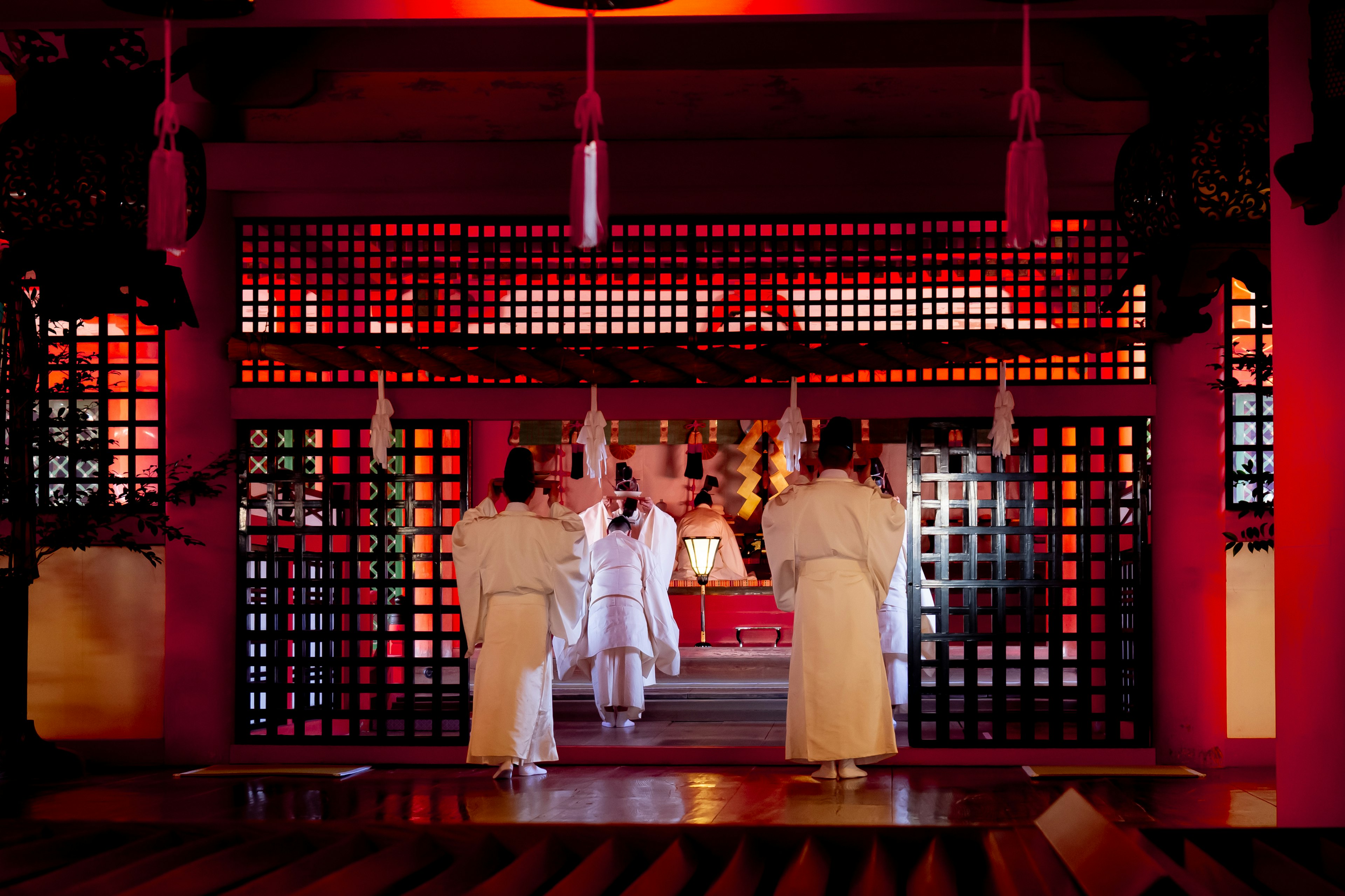 Three priests in white garments performing a ritual in a red shrine