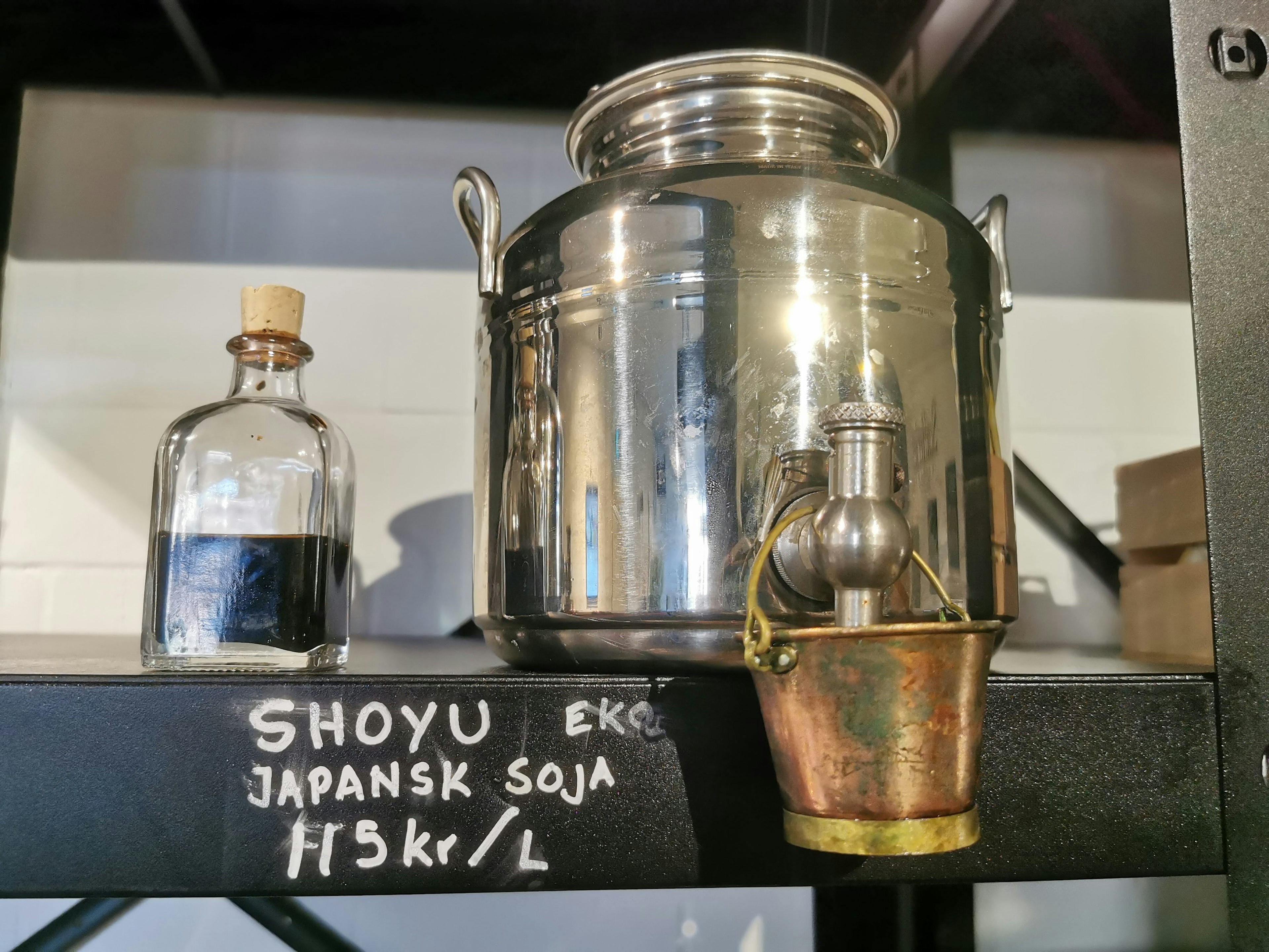 A stainless steel soy sauce container and a glass bottle on a shelf