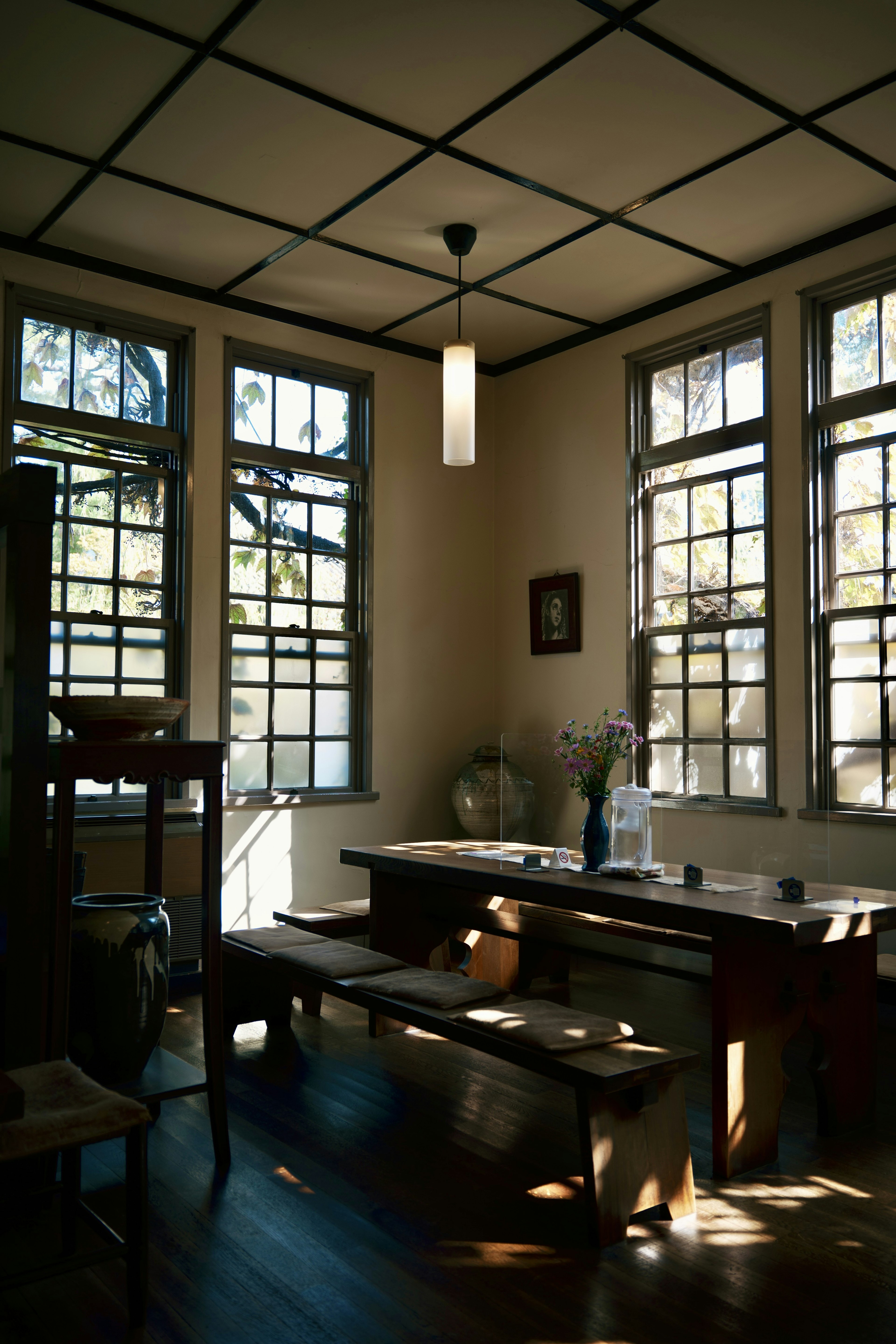 Área de comedor interior luminosa con grandes ventanas mesa de madera y bancos creando una atmósfera tranquila