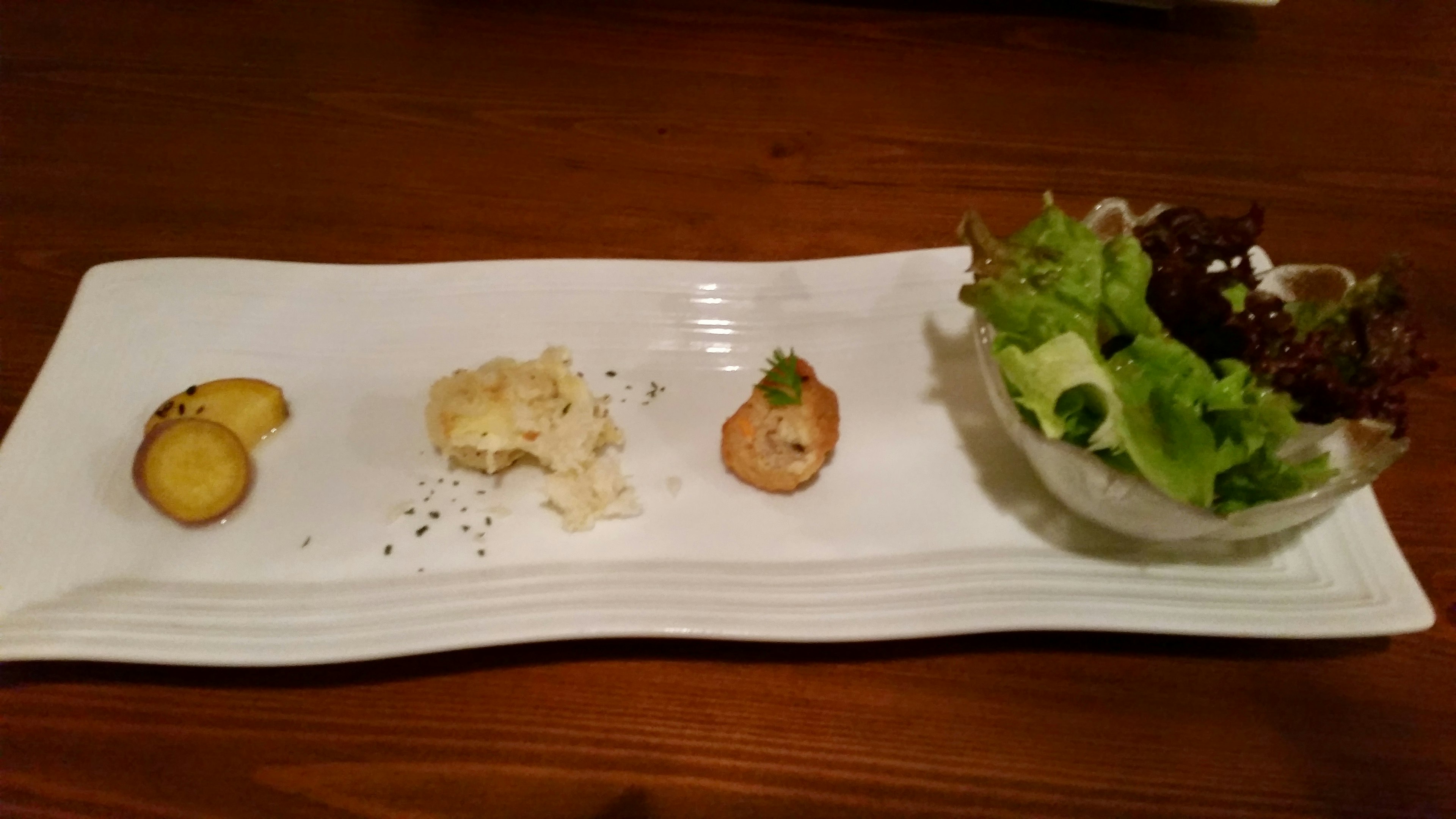 An appetizer platter on a white plate featuring salad, potato slices, and a creamy dish