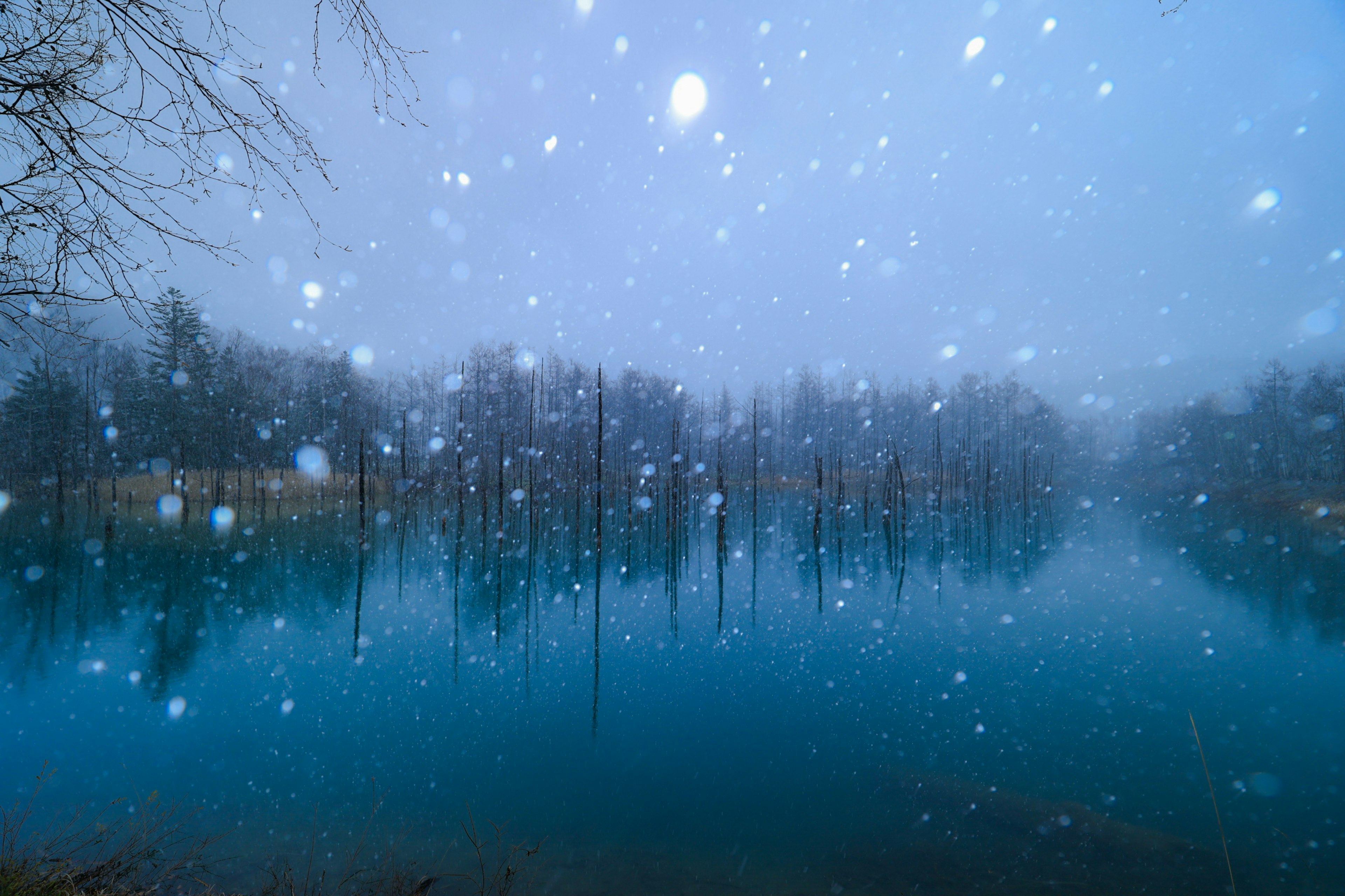 Snow falling over a tranquil lake with a blue surface