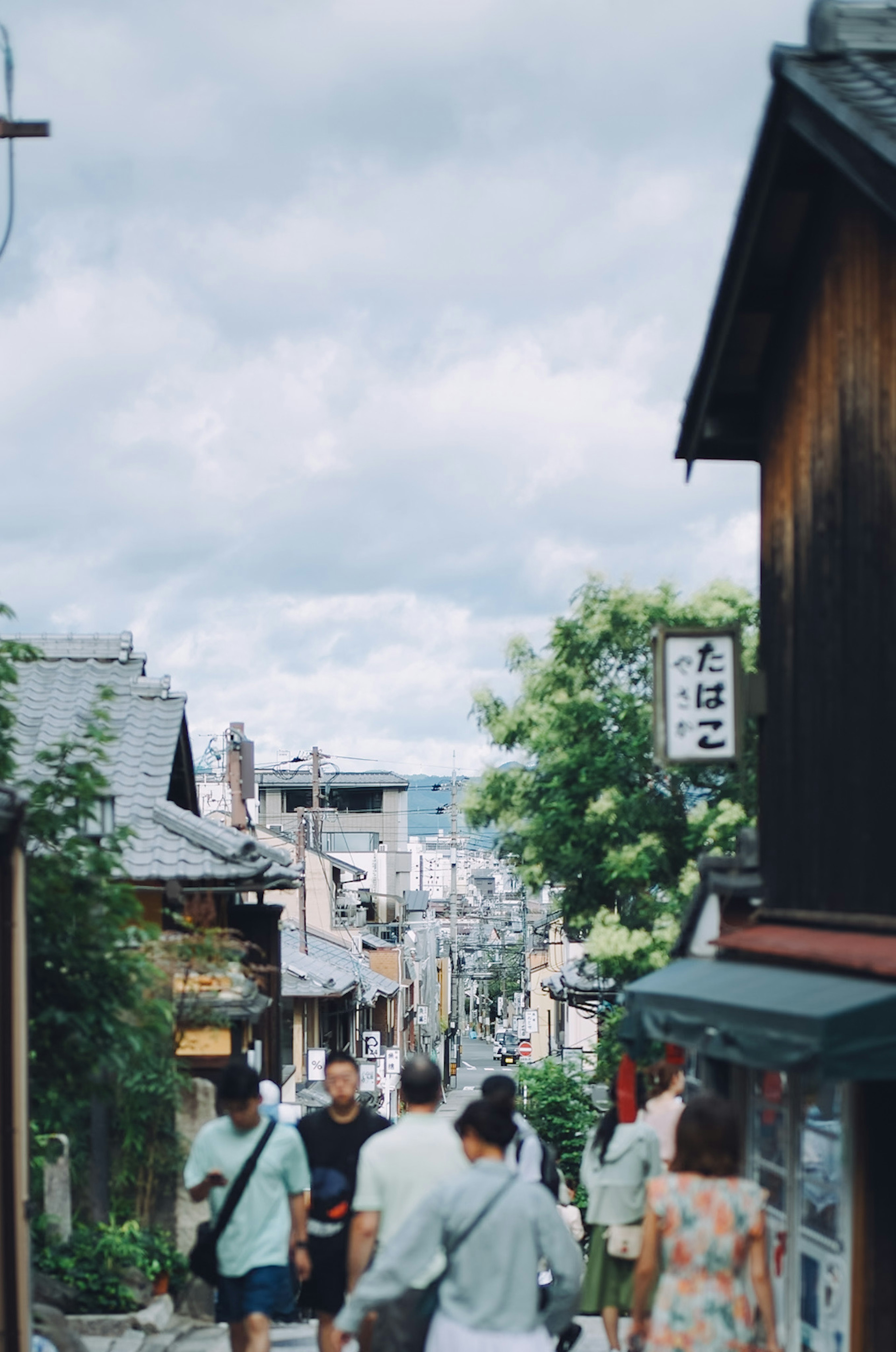 People walking down a hillside street in Kyoto with shops and greenery