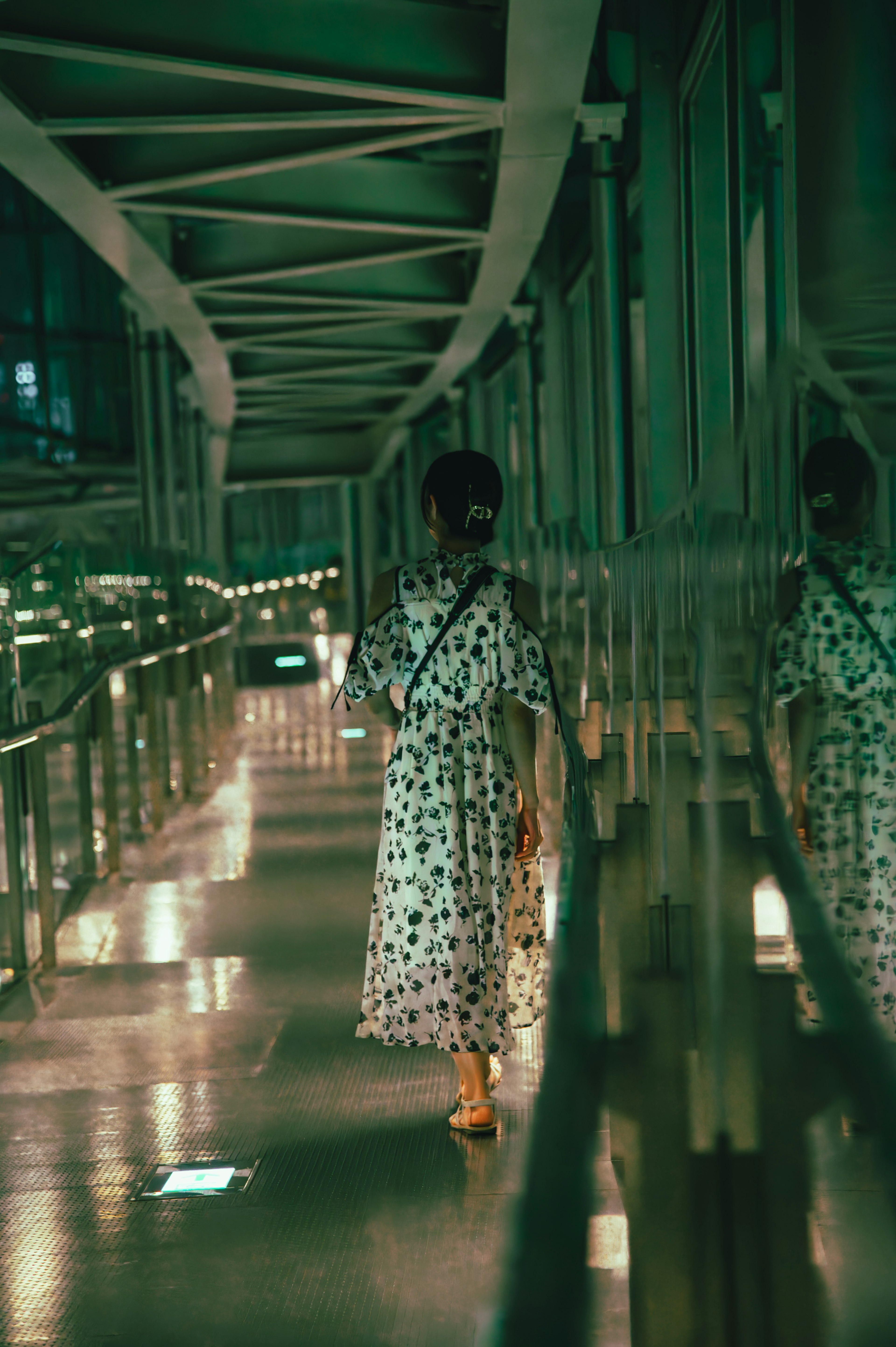 Mujer con vestido floral caminando en un pasillo iluminado en verde con reflejos