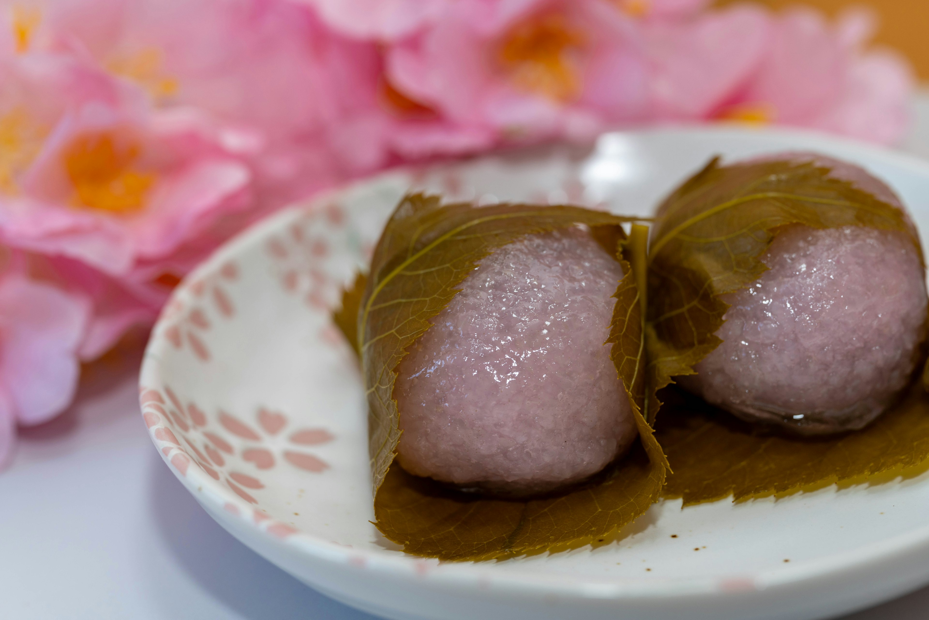 벚꽃 배경의 장식적인 접시에 놓인 두 개의 전통 일본 과자가 잎으로 싸여 있다