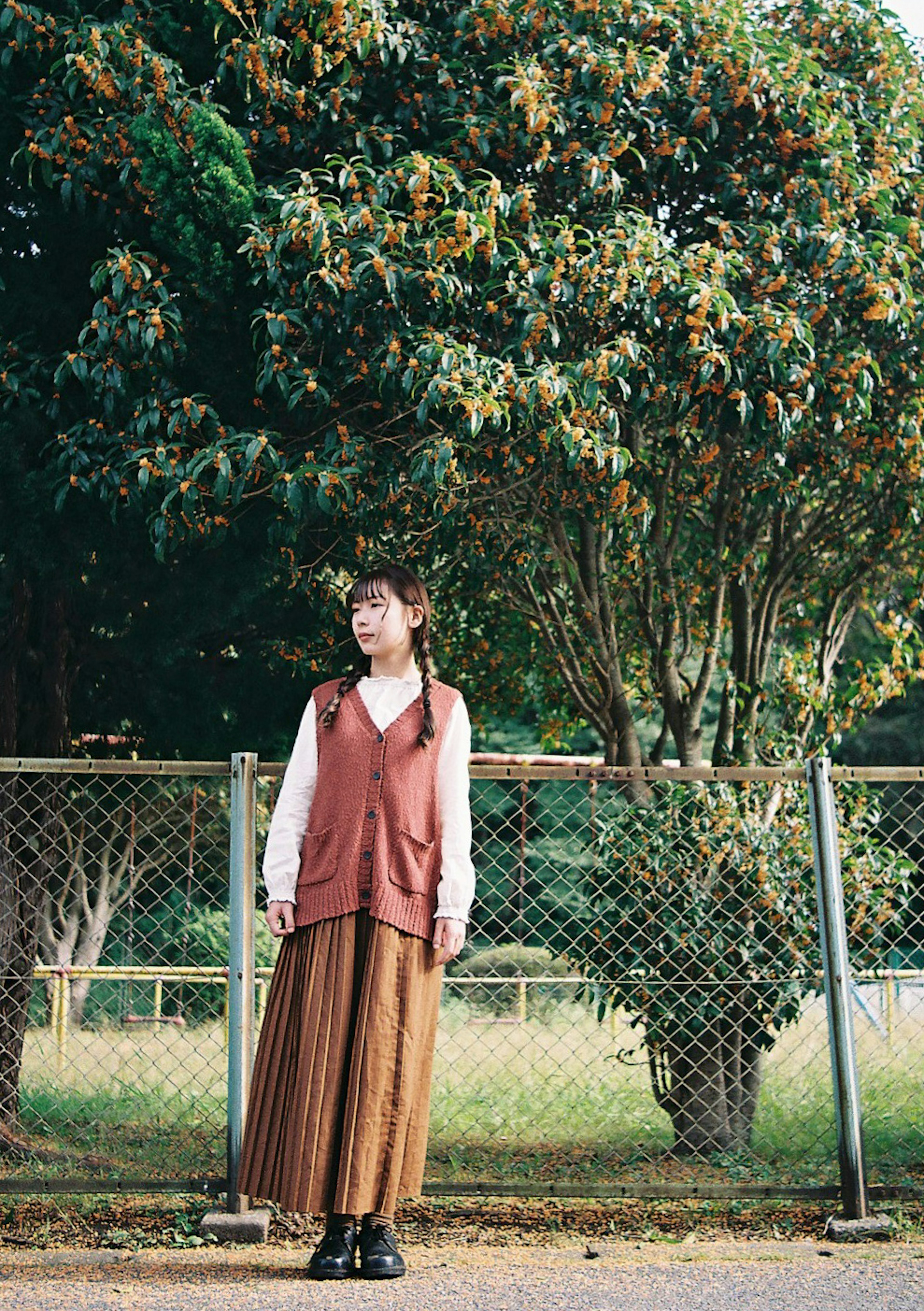 Une jeune femme en pull et jupe longue se tenant devant des arbres verts