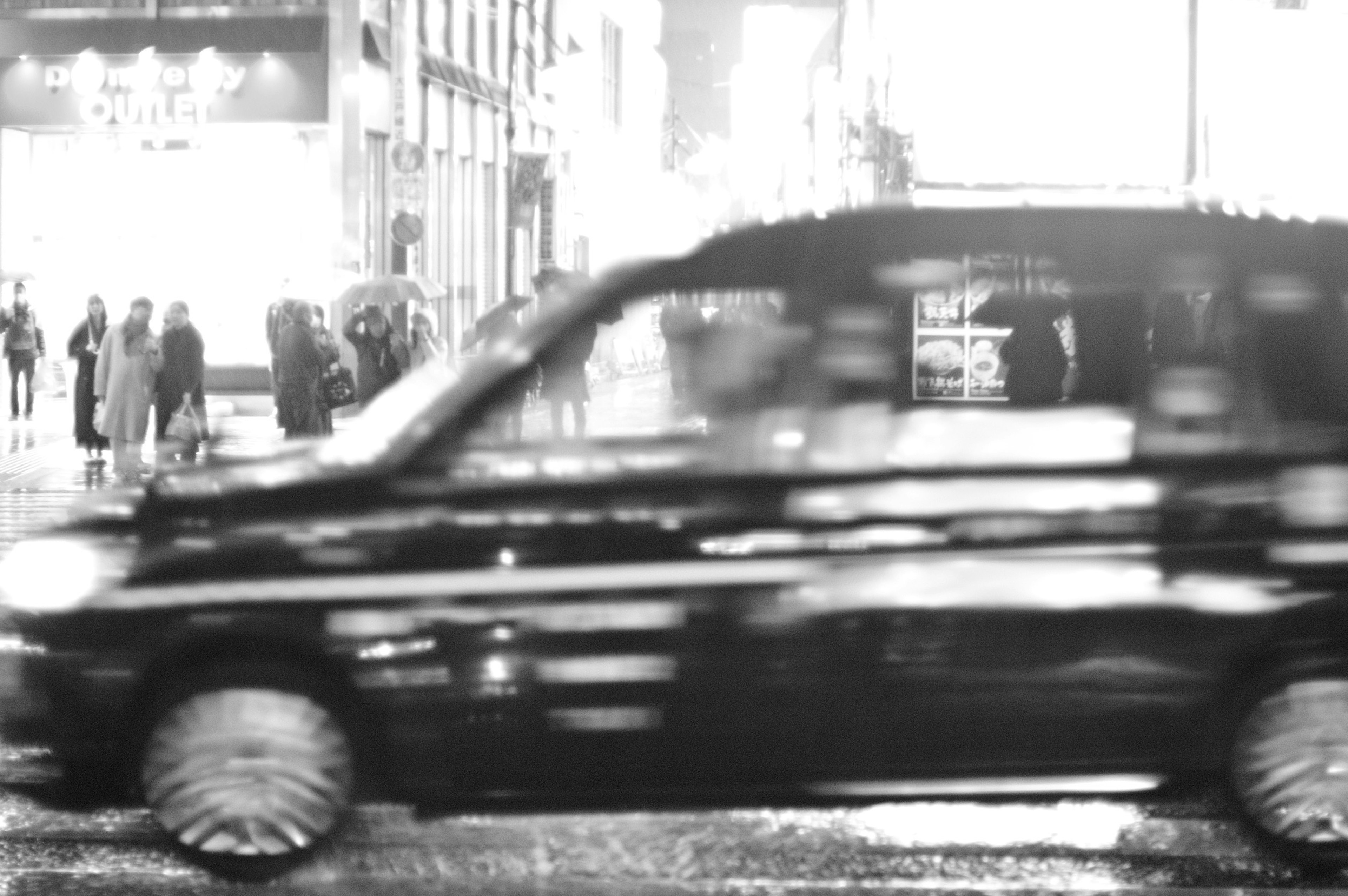 A taxi speeding through a rainy city street with blurred pedestrians