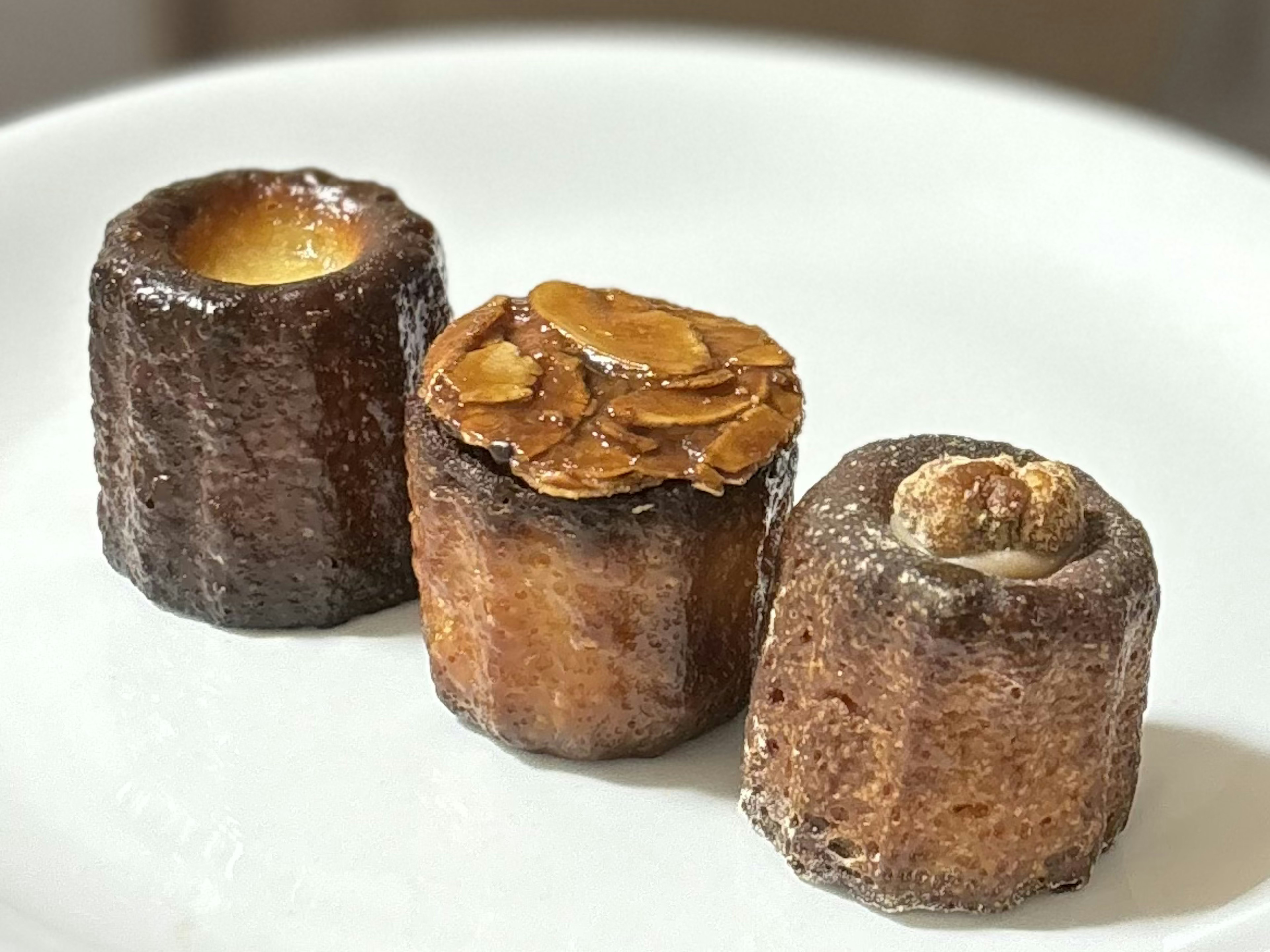 Trois canelés présentés sur une assiette blanche