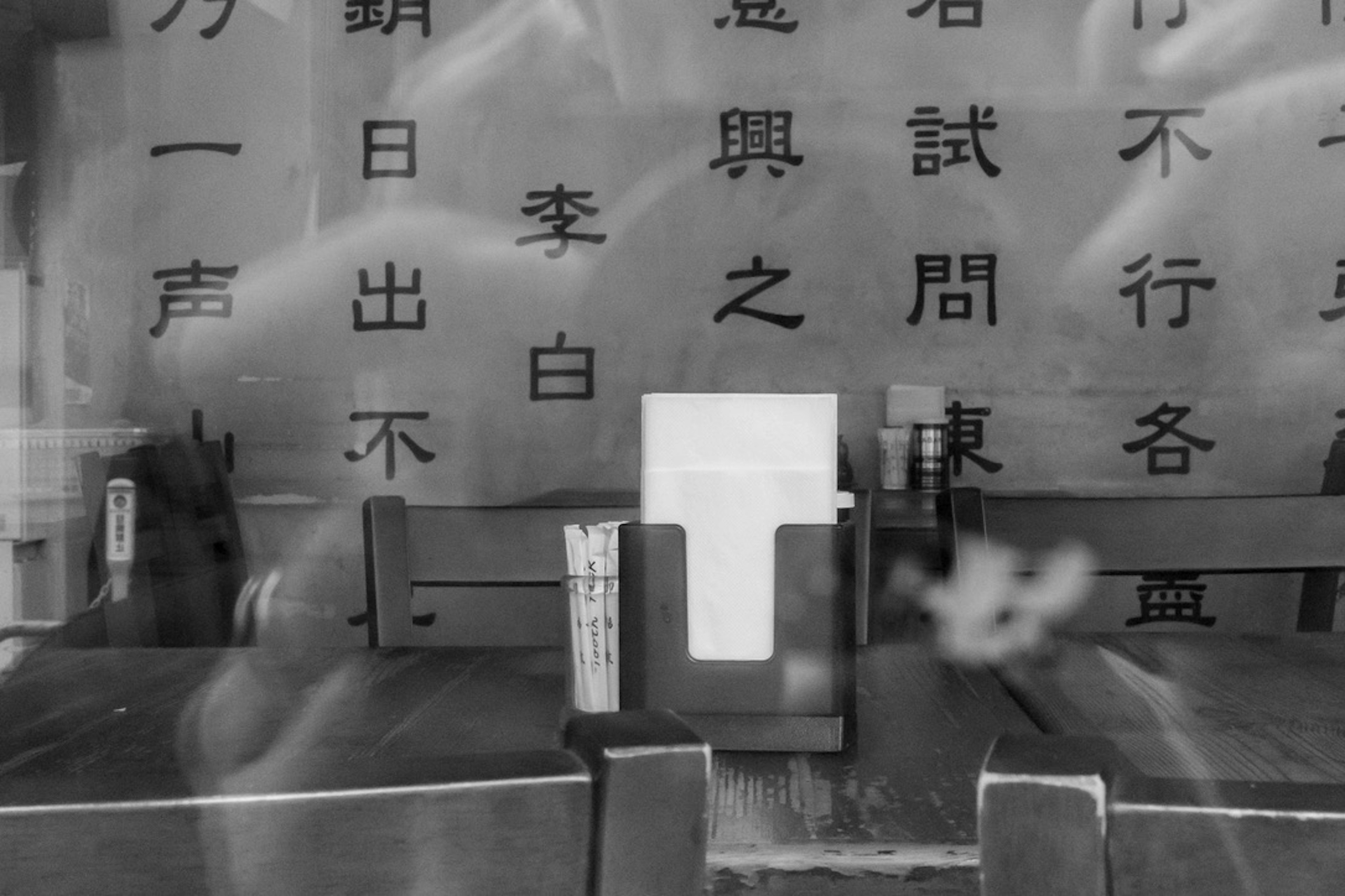 A white menu placed on a wooden table in front of a wall with black characters